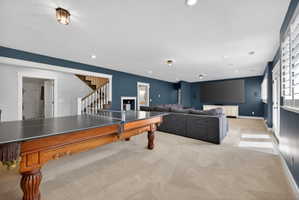 Spacious entertainment area featuring recessed lighting, a large screen, white plantation shutters, a staircase with wood banister, and built-in wall speakers