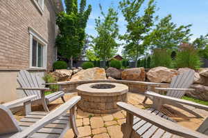 Paver patio featuring a built-in stone fire pit, stone retaining wall, and natural rock landscaping