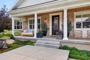 Brick exterior featuring a covered porch with white columns, concrete steps, a wood-paneled ceiling, and a dark-paneled door with decorative glass
