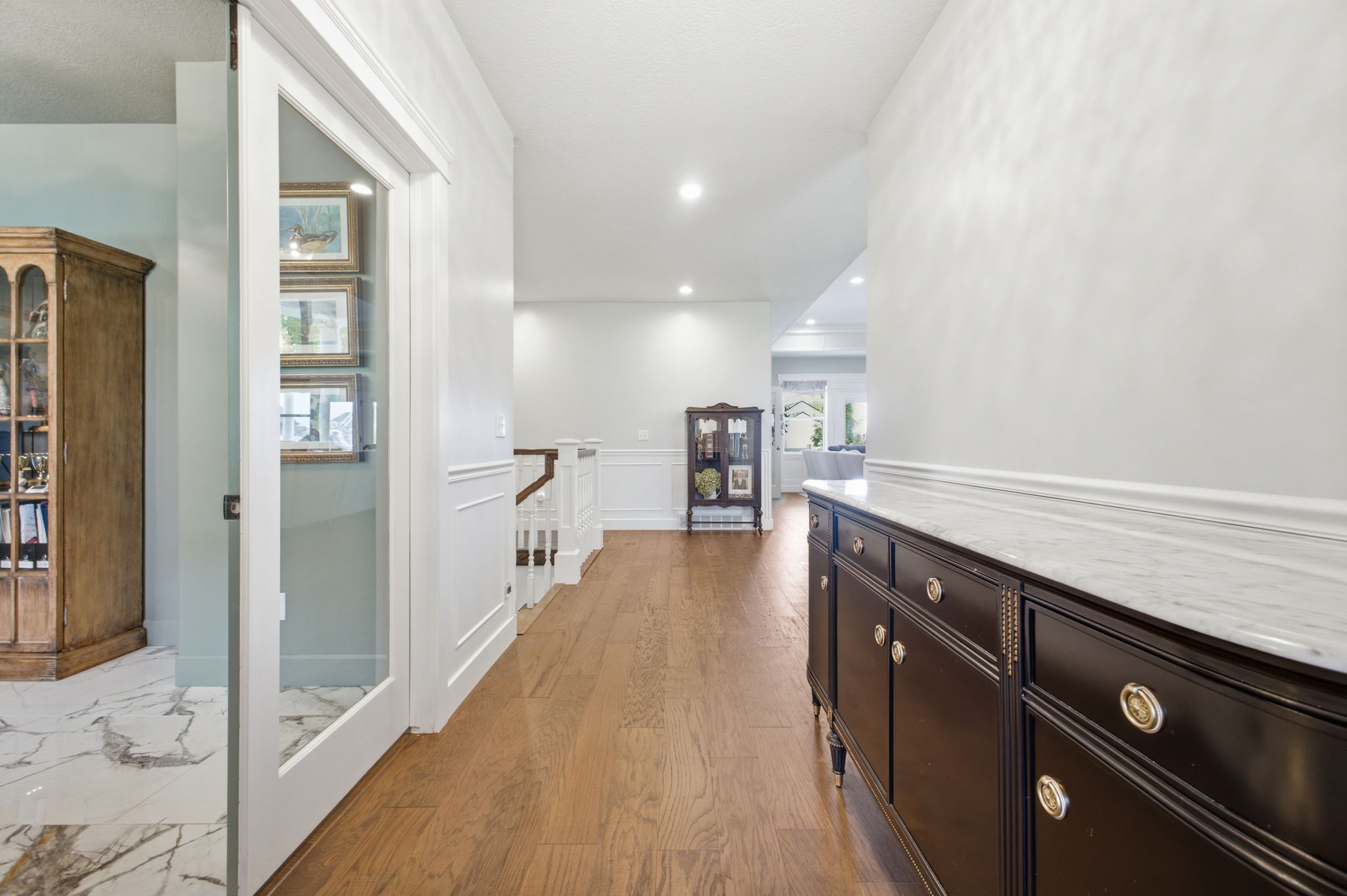 Hardwood flooring extends throughout the hallway, featuring white wainscoting and recessed lighting