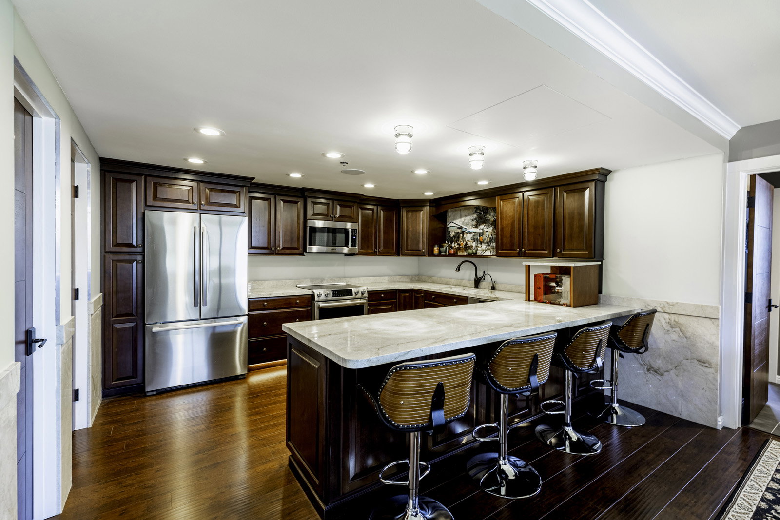 Spacious kitchen featuring rich wood cabinetry, stainless steel appliances, light-toned countertops, a multi-person island, and dark wood-finish flooring