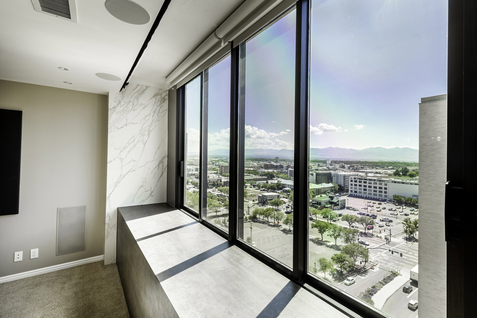 Floor-to-ceiling windows with roller shades offer expansive city and mountain scenery