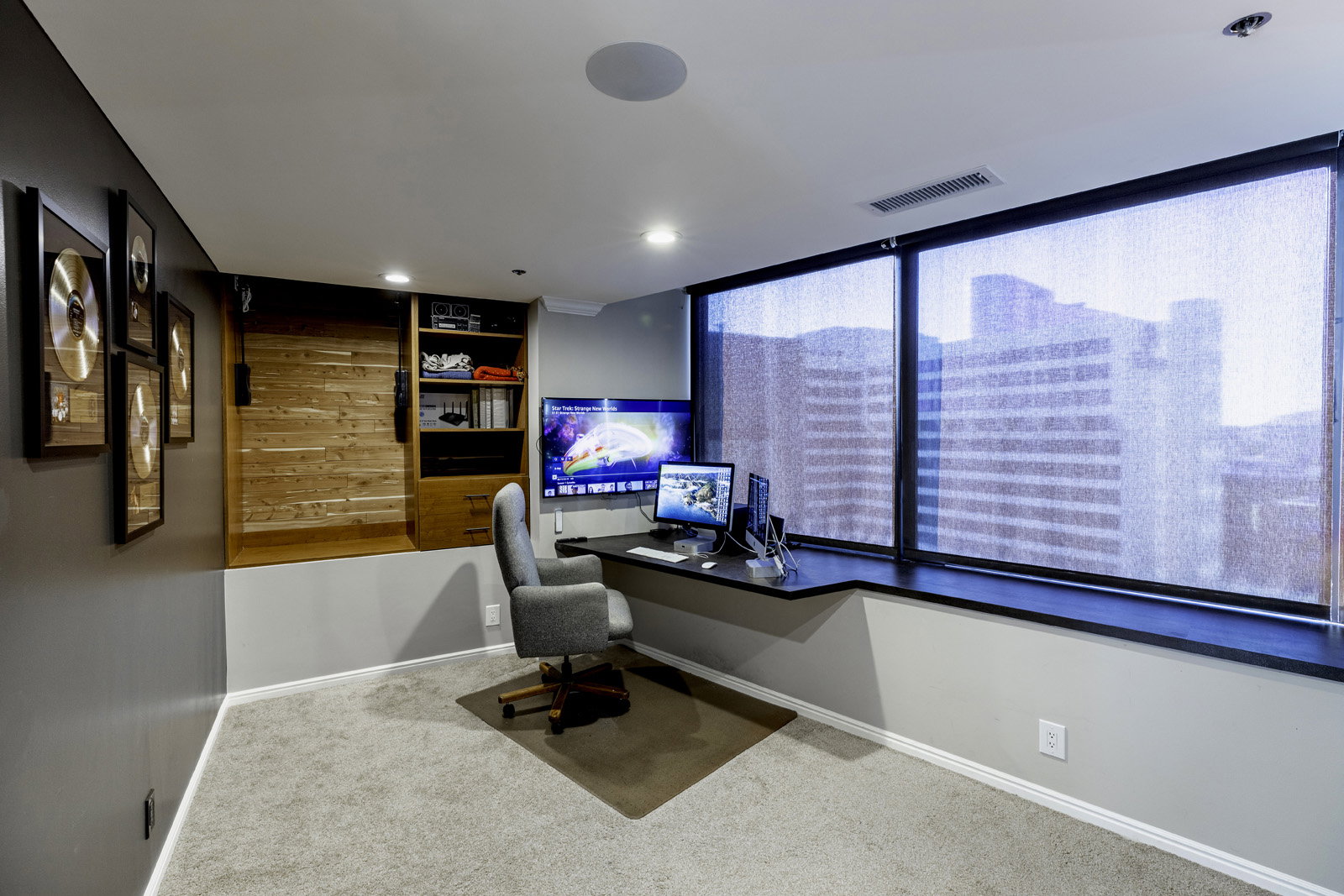 Dedicated workspace featuring a built-in desk, expansive windows with roller shades, recessed lighting, and a built-in storage unit with a wood-finish barn door