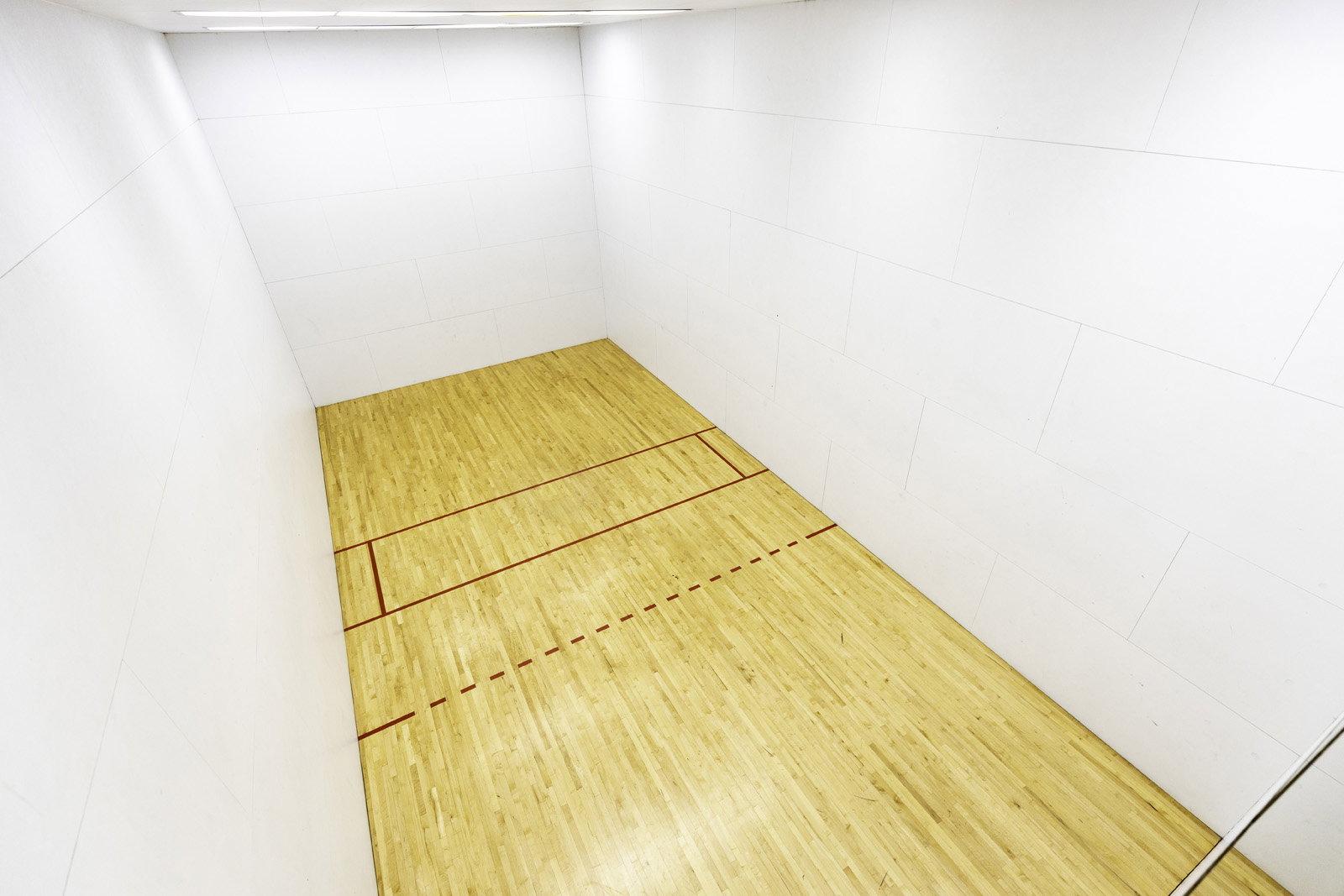 Indoor racquetball court with light wood-finish flooring and marked red lines