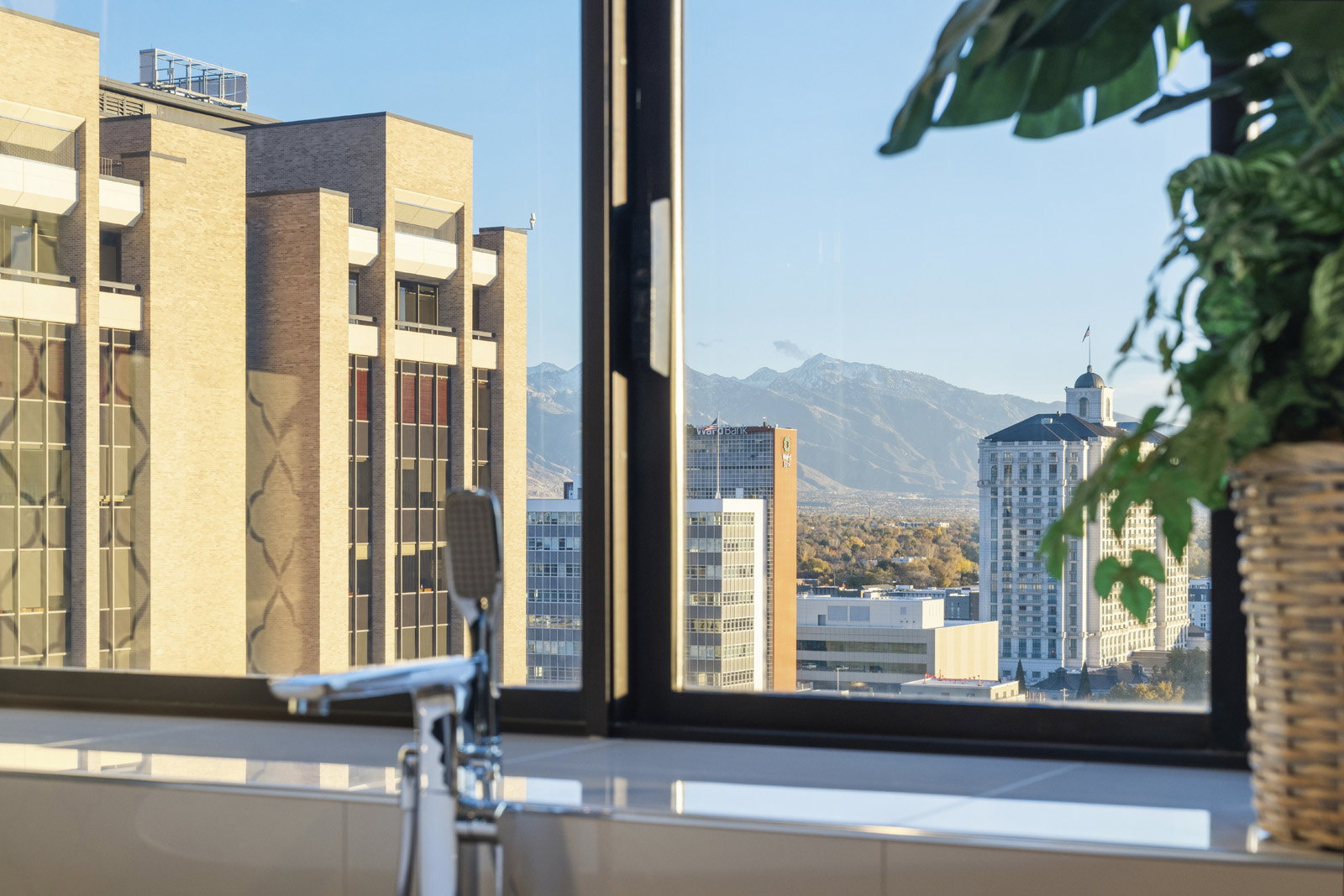 Soaking tub with floor-mounted chrome faucet, set against a expansive window offering cityscape and mountain scenery