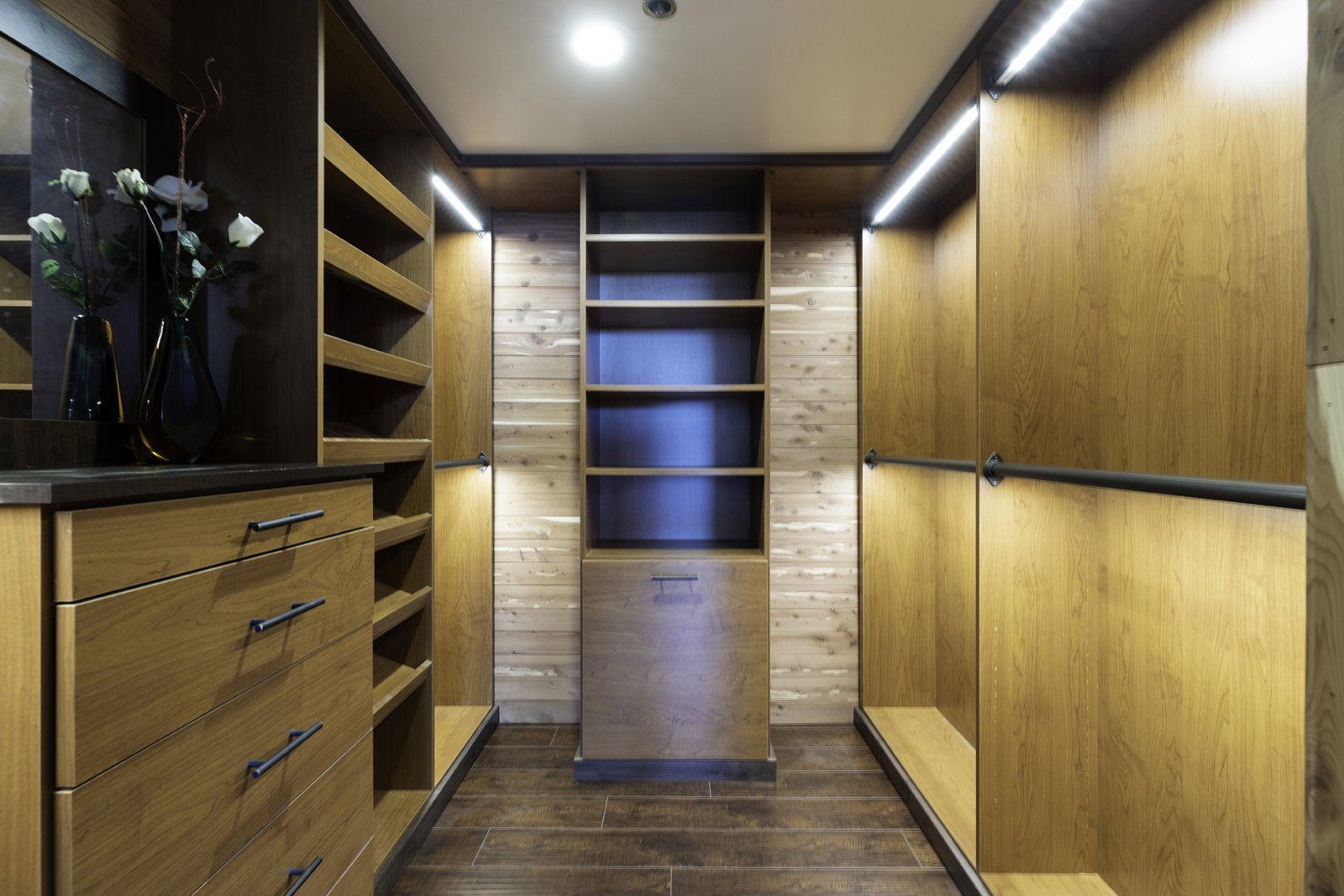 Custom walk-in closet featuring wood-finish cabinetry, built-in shelving, integrated lighting, dark wood-finish flooring, and a stone-look countertop
