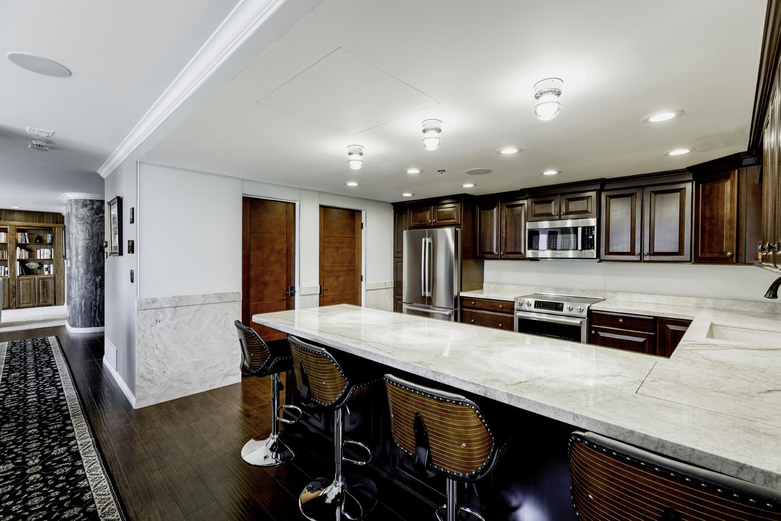 Gourmet kitchen featuring rich wood cabinetry, stainless steel appliances, a spacious central island with an integrated sink, and recessed lighting