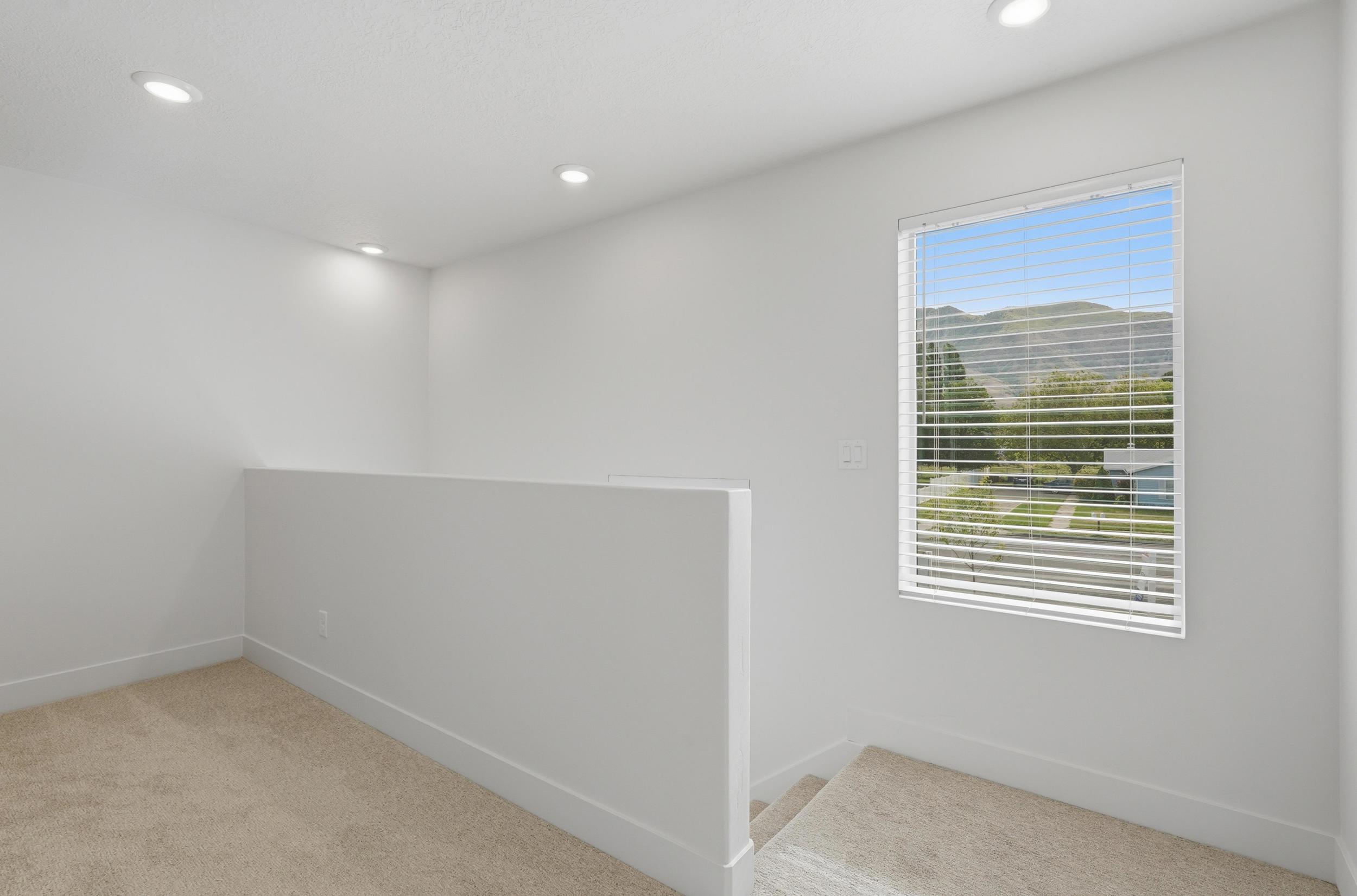 Carpeted upper-level space featuring a contemporary half-wall, recessed ceiling lighting, and a window with horizontal blinds offering a mountain and neighborhood backdrop