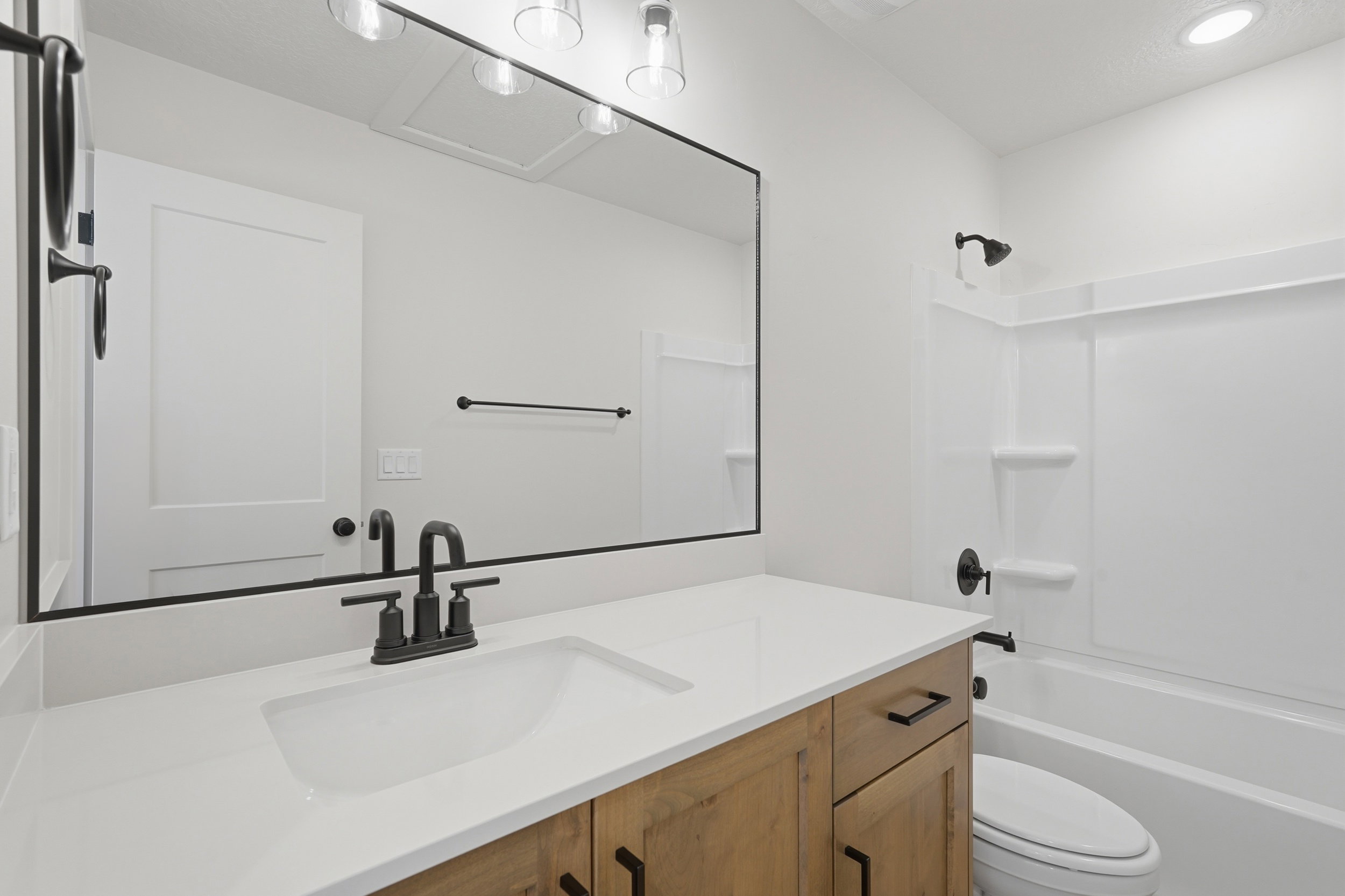 Bathroom featuring a wood-finish vanity with a white countertop and integrated sink, matte black faucet hardware, and a framed mirror with integrated lighting