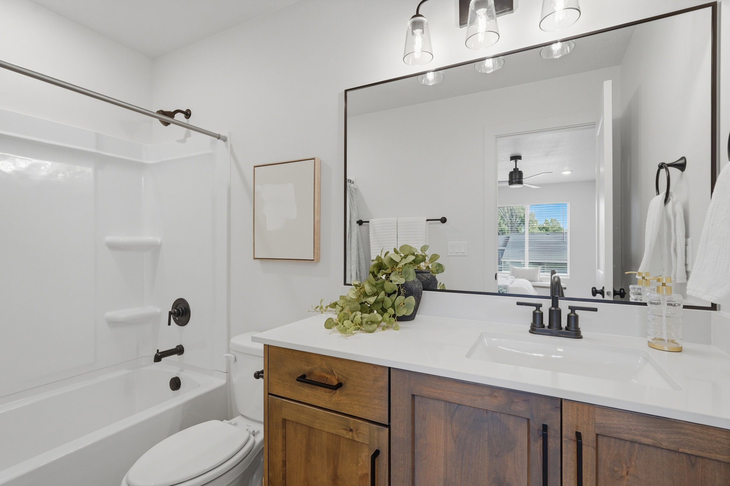 Bathroom featuring a wood-finish vanity with an integrated white sink, a large framed mirror, and a white tub/shower combination with black fixtures