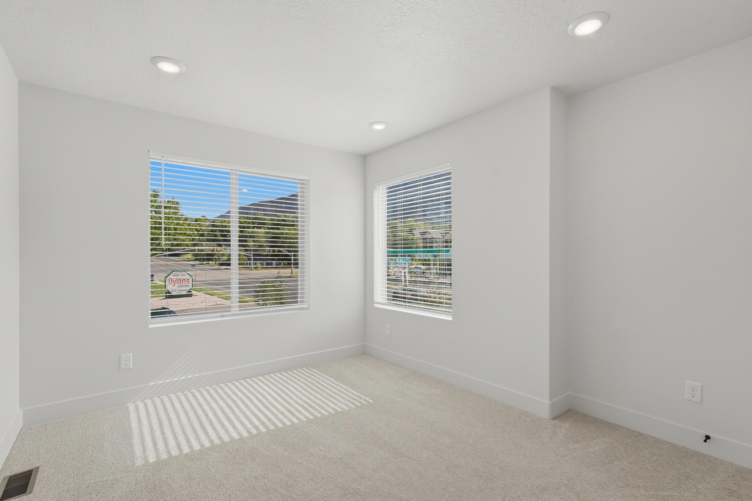 Bright room featuring recessed lighting, a large window with blinds, a second window, neutral carpeting, and white baseboards