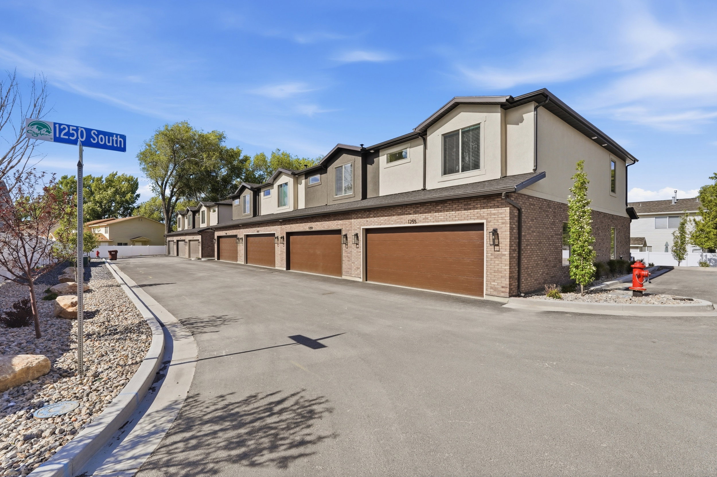 Townhome exterior featuring a combination of brick and stucco siding, individual garage doors with a wood-grain finish, dark-framed windows, and a paved driveway