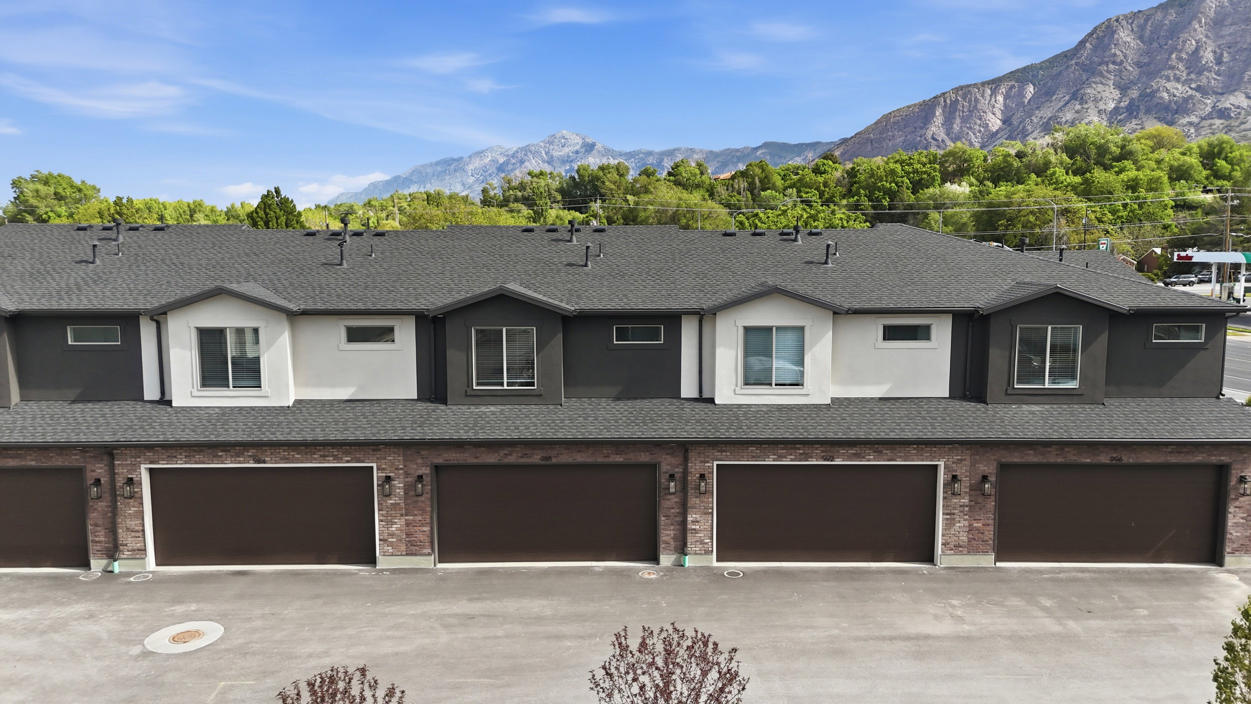 Modern townhome exterior featuring individual attached garages, a dark shingle roof, and a combination of brick and stucco siding