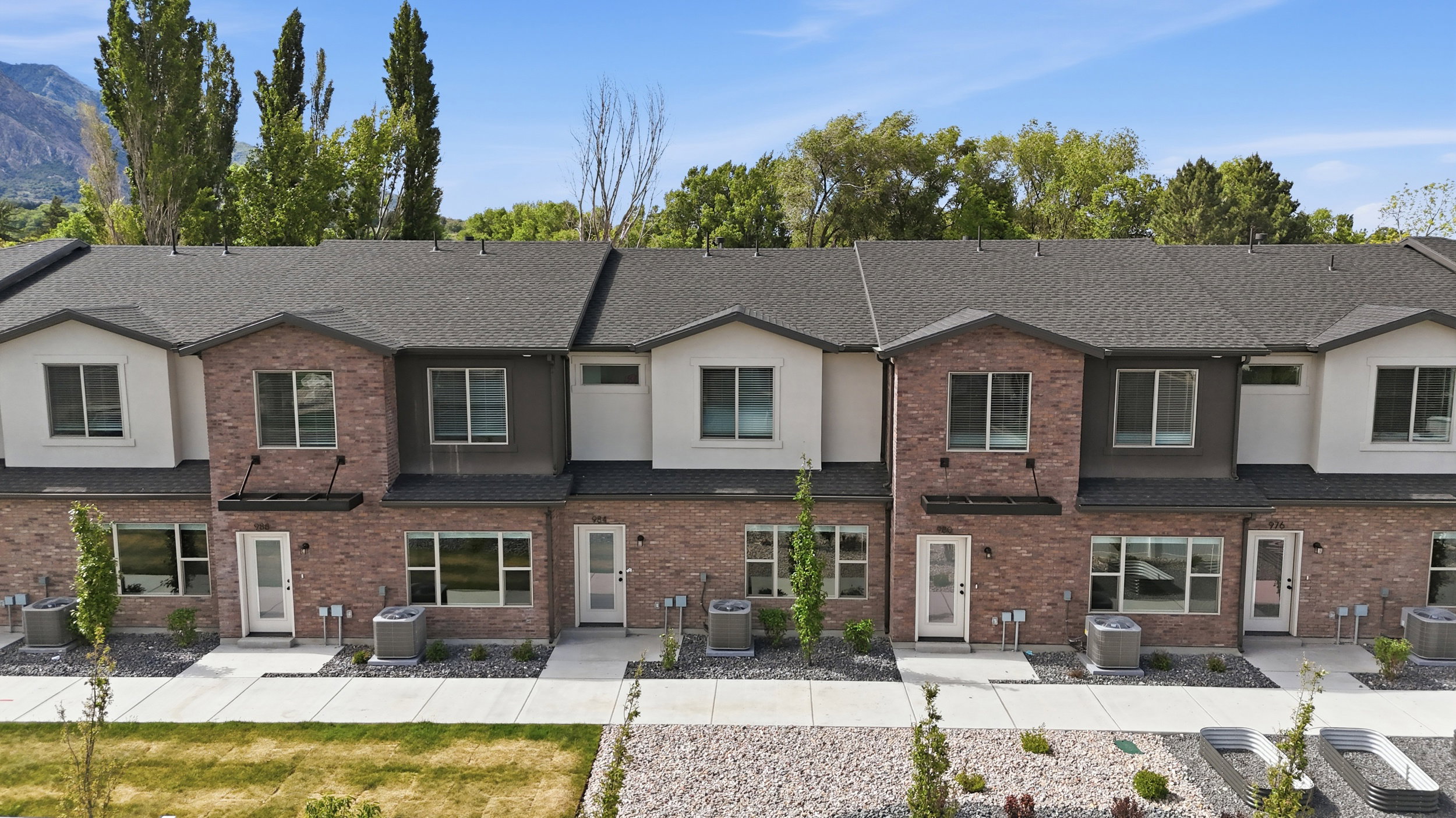 Contemporary townhome exteriors featuring brick and stucco finishes, dark asphalt shingle roofing, multiple windows, and individual entry doors