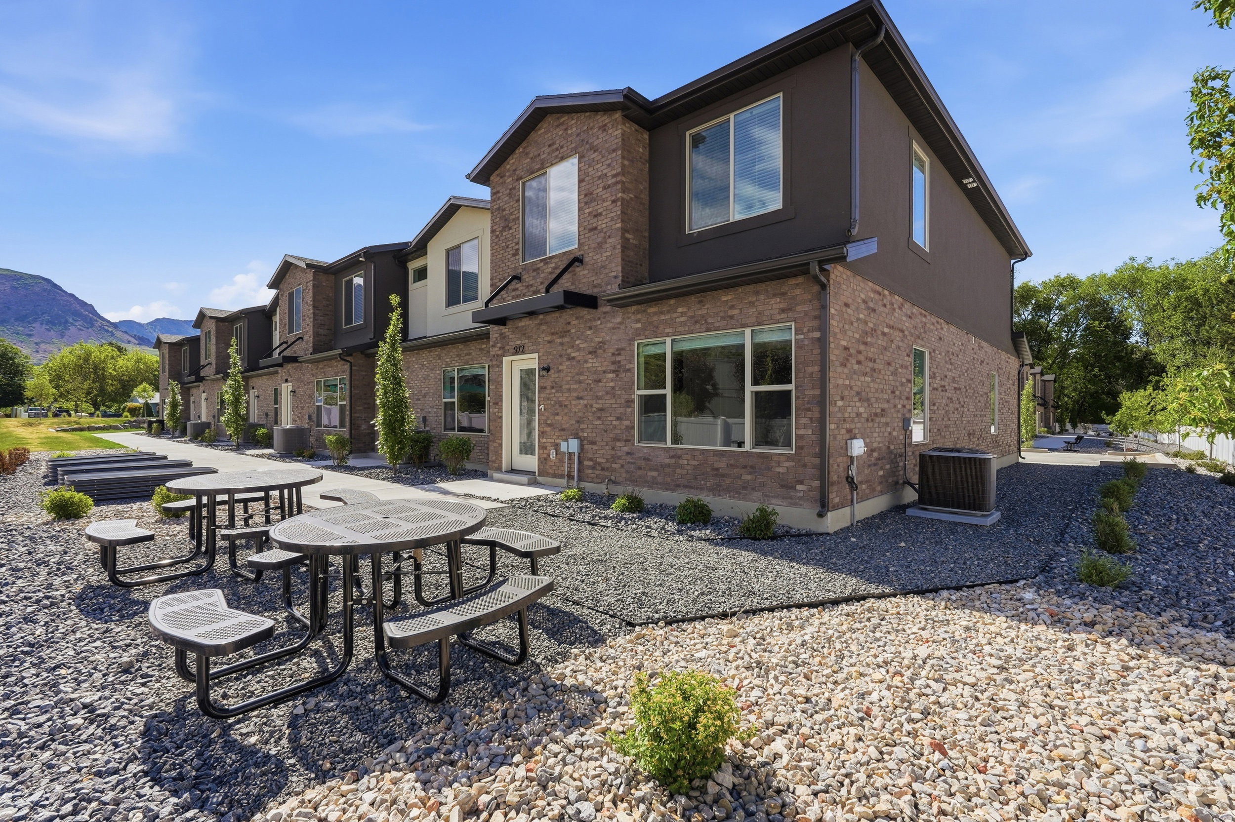 Townhome exterior featuring brick and dark siding, multiple windows, and a paved walkway leading to the entrance