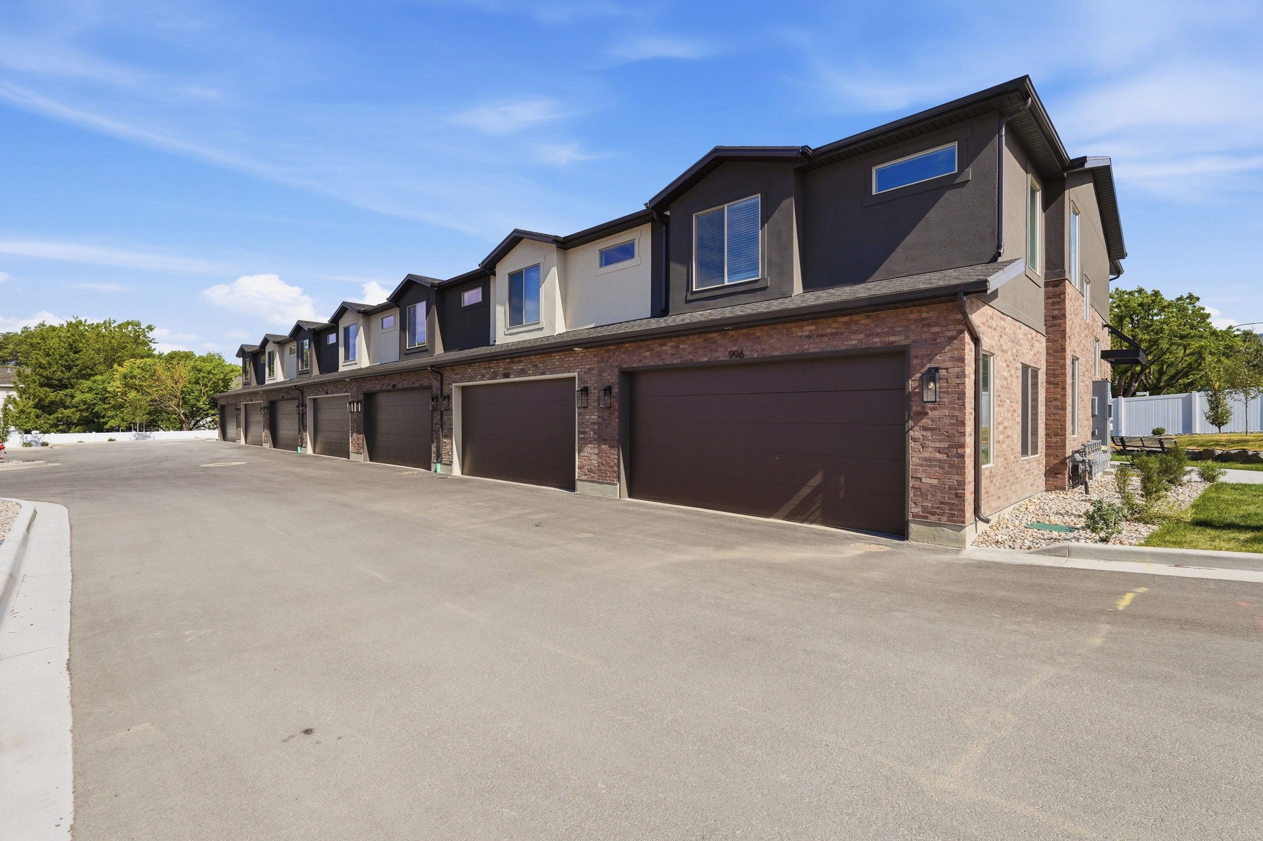 Multi-story exterior featuring a brick and stucco facade, individual garage bays, multiple windows, and exterior lighting fixtures
