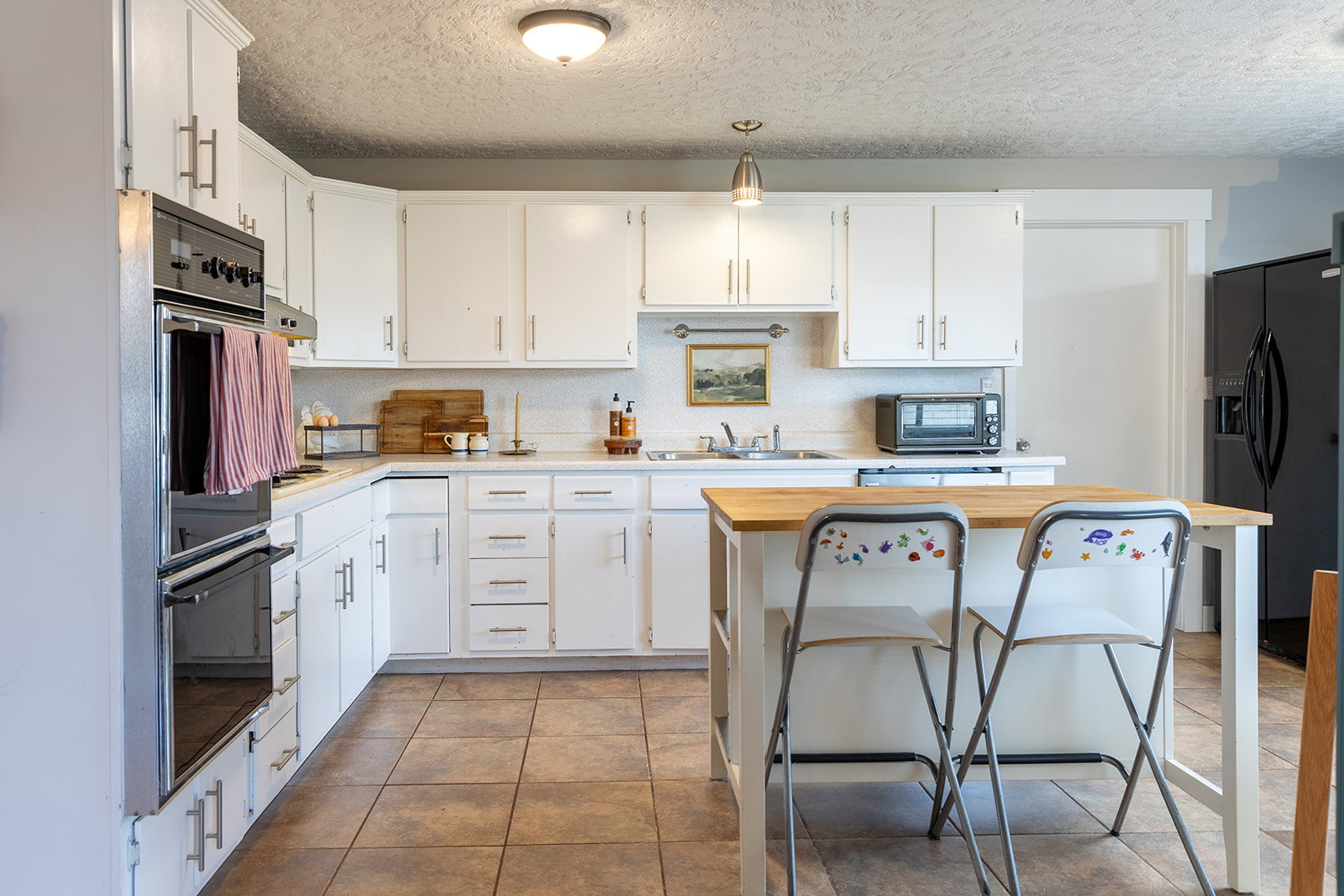 Kitchen featuring white cabinetry with silver hardware, an integrated double oven, a white tile backsplash, and light-toned tile flooring