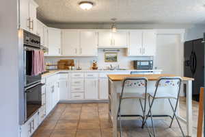 Kitchen featuring white cabinetry with silver hardware, an integrated double oven, a white tile backsplash, and light-toned tile flooring