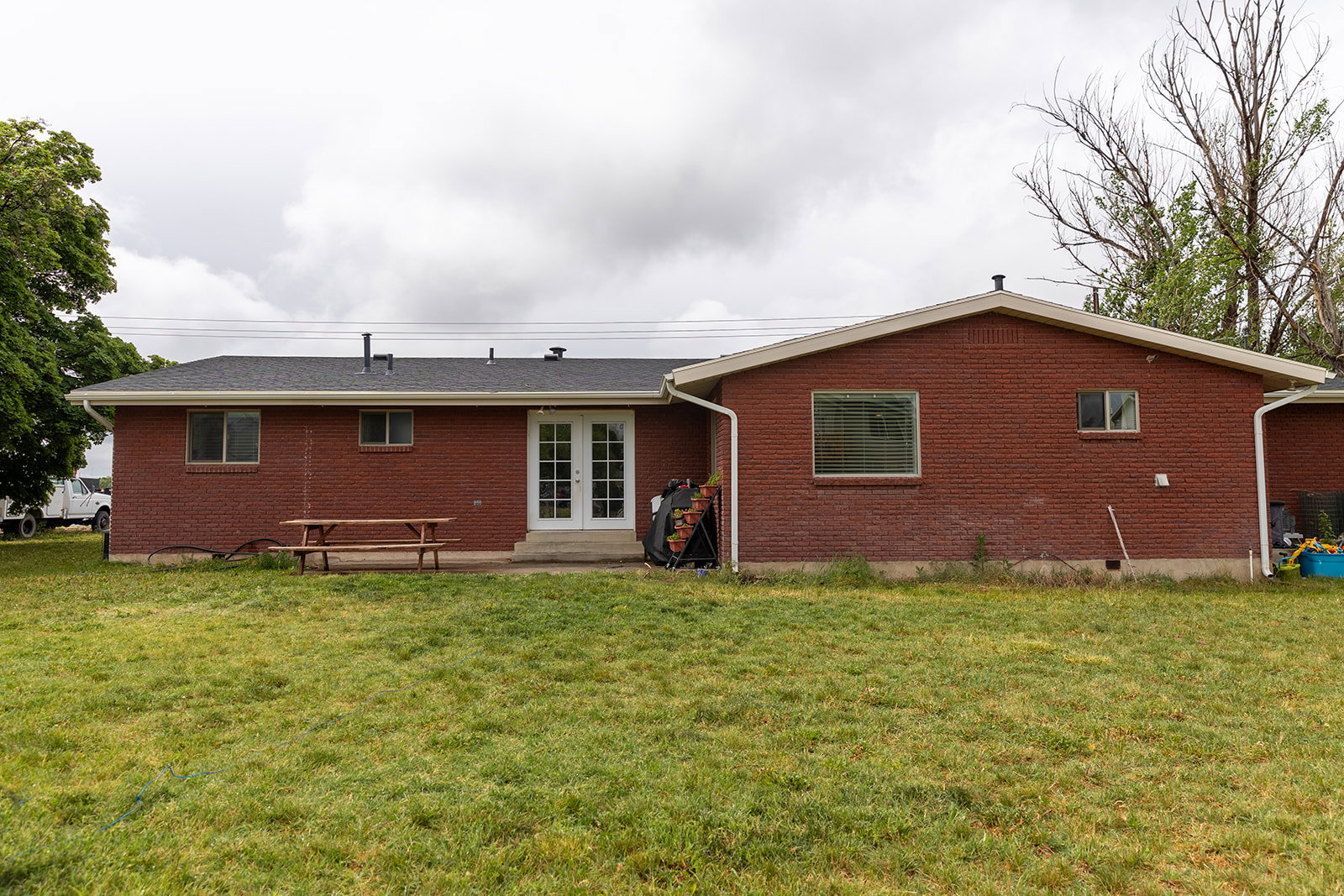 Red brick exterior featuring a black shingle roof, white trim, and white double French doors
