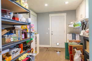 Utility space featuring wood-finish flooring, white paneled door with pet access, recessed lighting, and built-in upper cabinetry