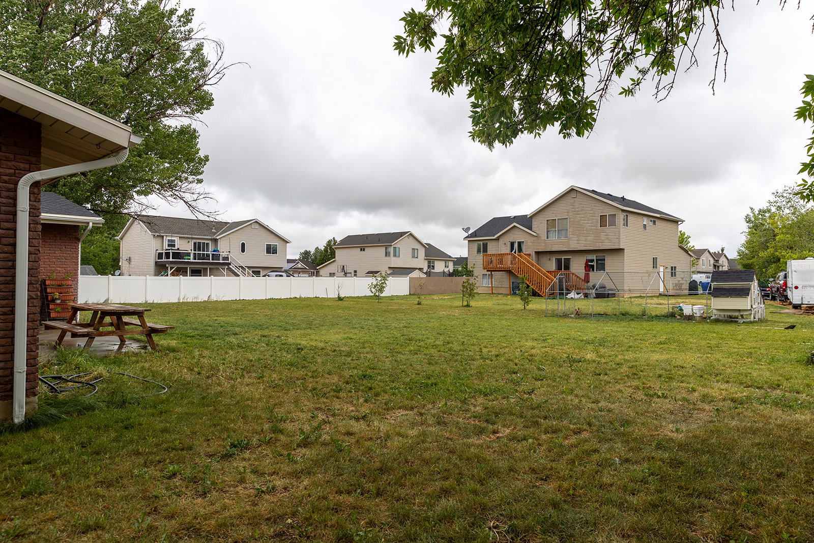 Spacious backyard featuring a large grassy area, a white privacy fence, and a multi-level wood deck with stairs