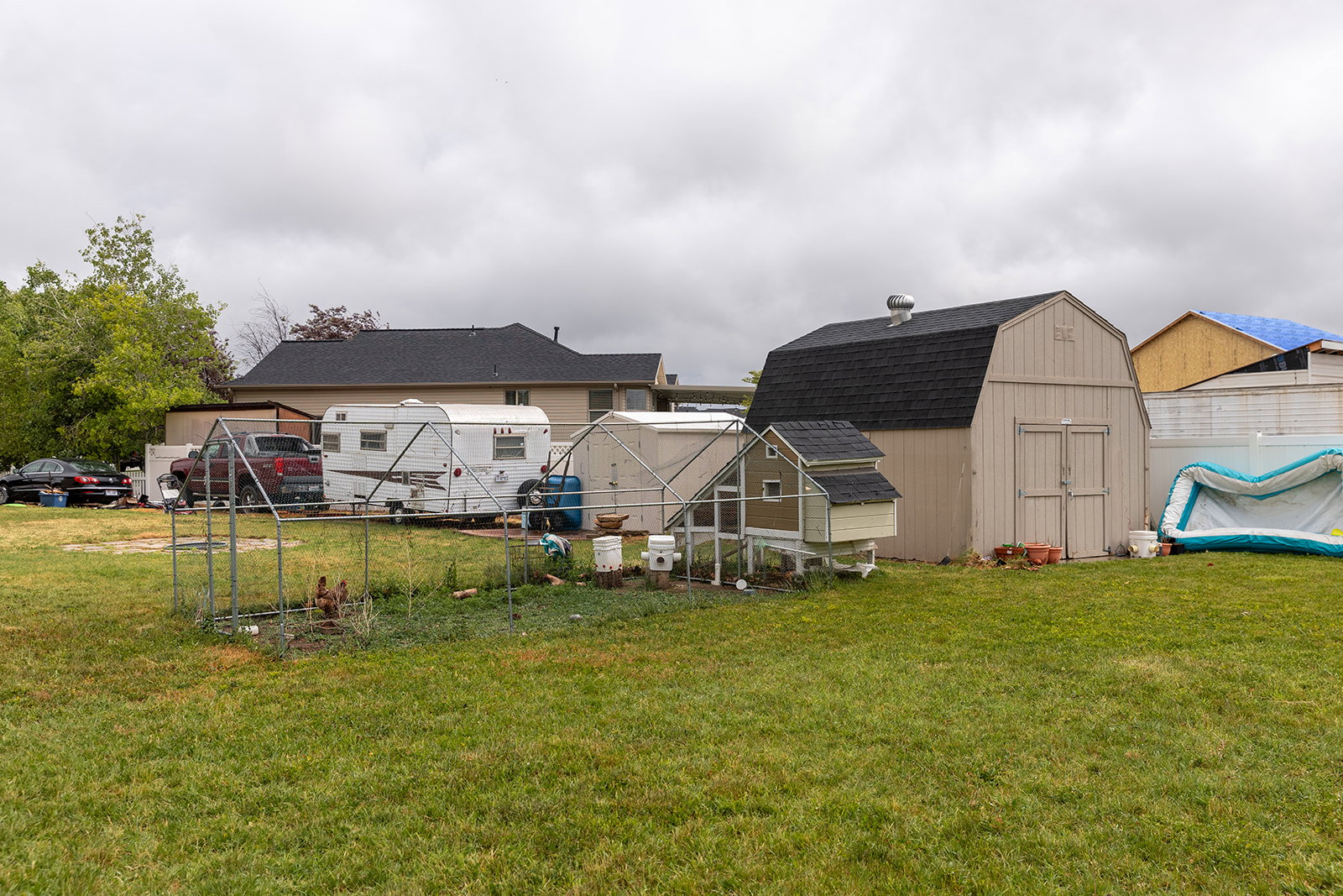 Expansive grassy lawn area featuring a gambrel-roofed shed with double doors, a chicken coop, and a fenced enclosure