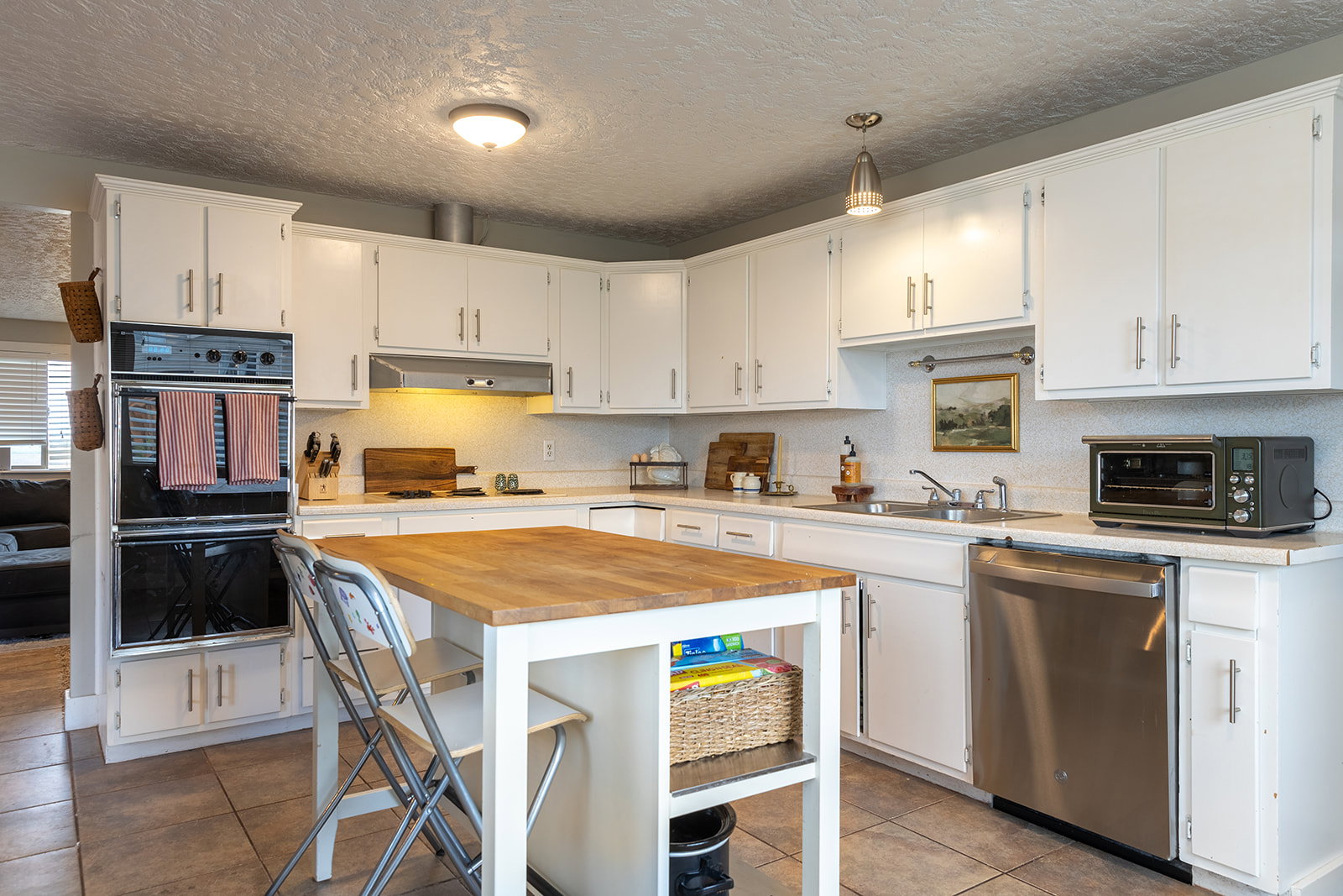 Bright kitchen featuring white cabinetry, a built-in double oven, a stainless steel dishwasher, a butcher block island, and tile flooring