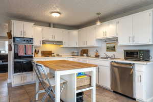 Bright kitchen featuring white cabinetry, a built-in double oven, a stainless steel dishwasher, a butcher block island, and tile flooring