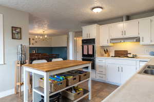 Kitchen featuring white cabinetry, double wall ovens, built-in range hood, and tile flooring