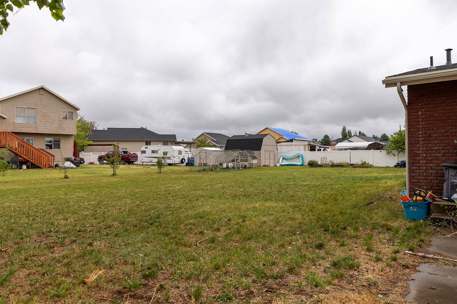 Expansive grassy yard area featuring a partial brick exterior, white privacy fencing, and a separate storage shed