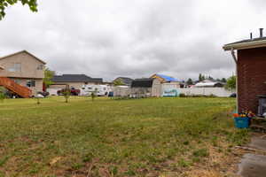Expansive grassy yard area featuring a partial brick exterior, white privacy fencing, and a separate storage shed