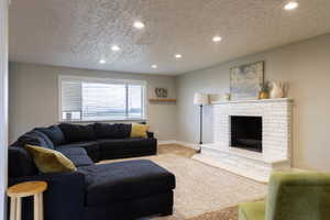 Spacious living area featuring a white brick fireplace with a hearth, recessed ceiling lighting, light gray wall paint, and a large window with blinds