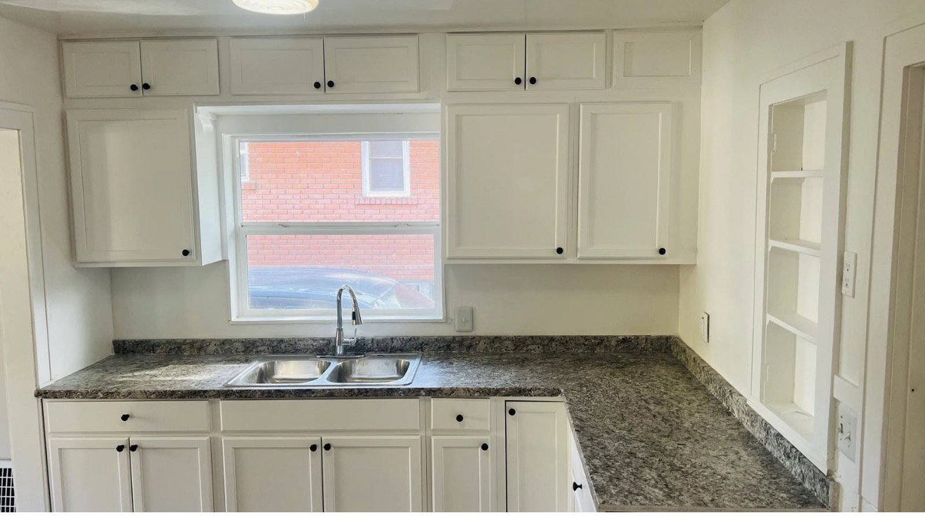 Kitchen featuring white shaker-style cabinetry, a double basin stainless steel sink with a gooseneck faucet, and mottled gray countertops