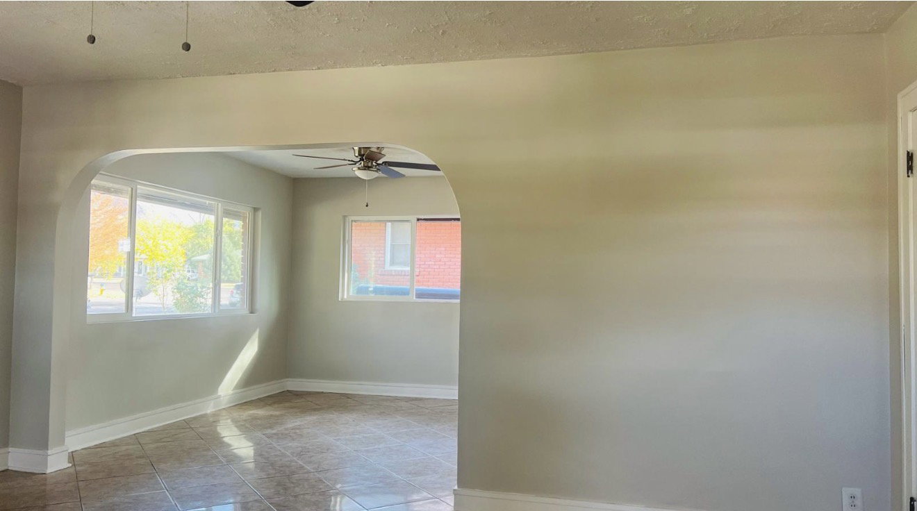 Arched doorway leading into a room with large windows, tiled flooring, and a ceiling fan