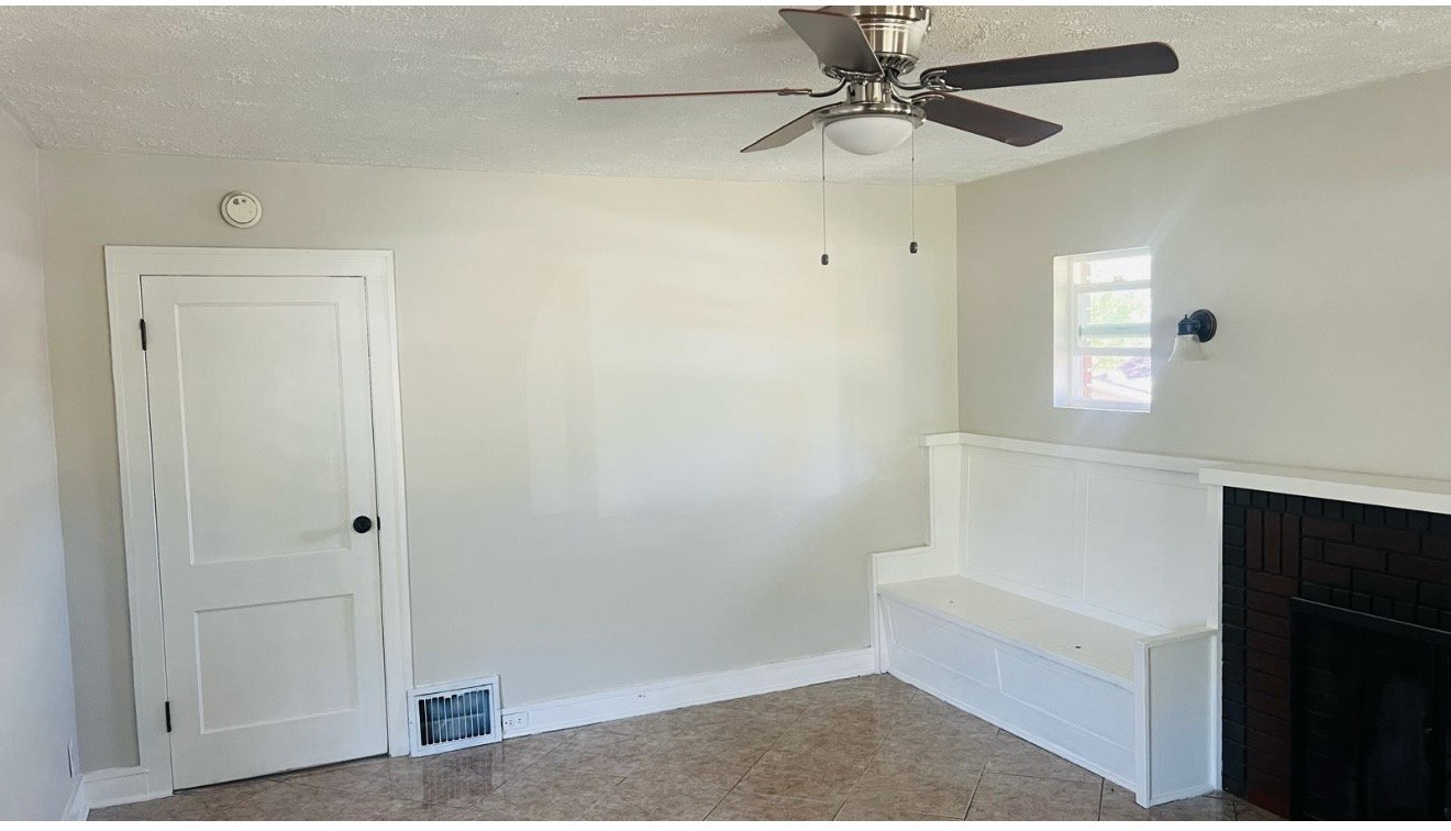 Room featuring a built-in bench with storage, a dark brick fireplace, a ceiling fan with light fixture, and tile flooring