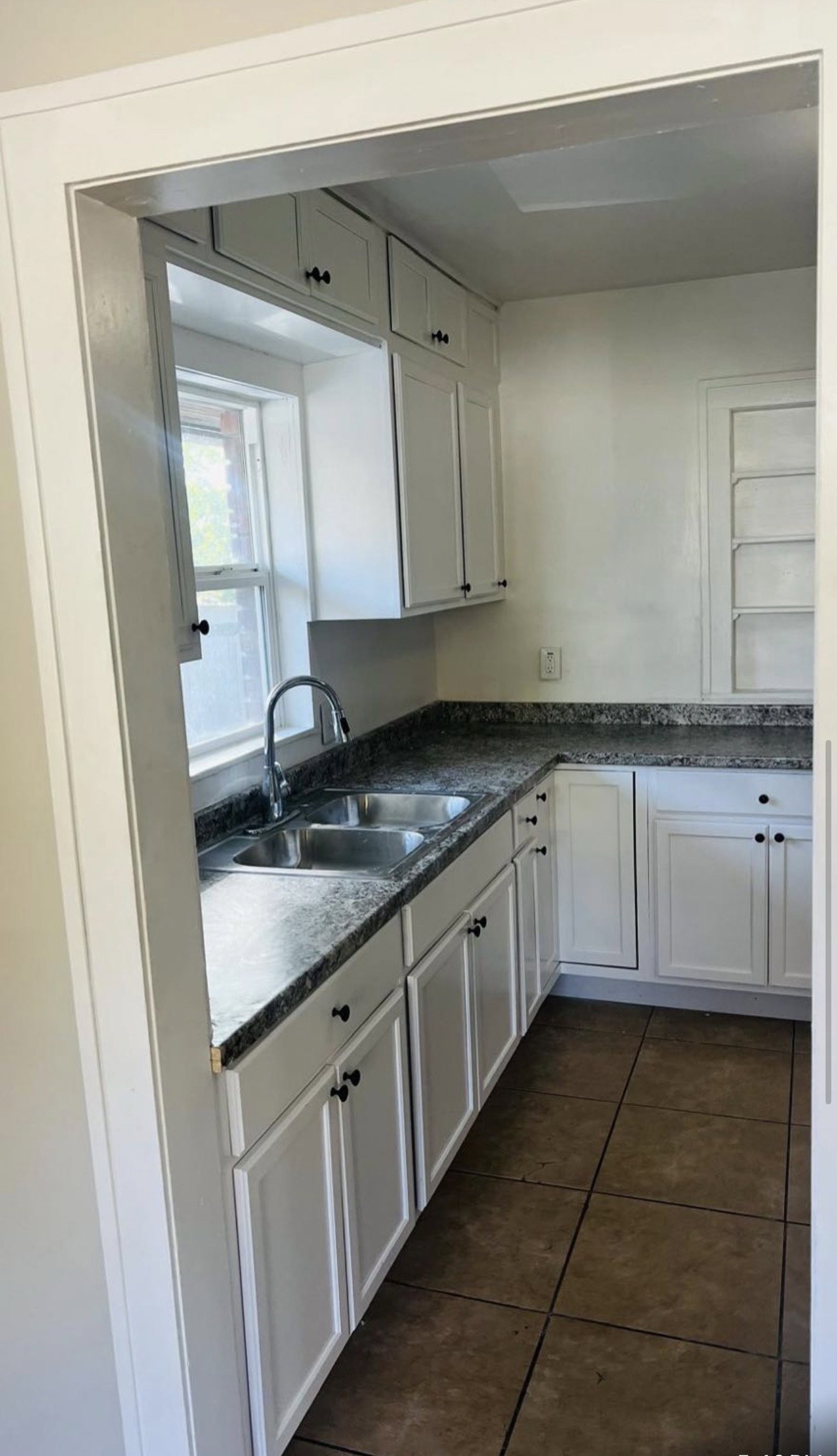 Kitchen featuring white cabinetry with black hardware, a stainless steel double basin sink, dark patterned countertops, and square floor tiles