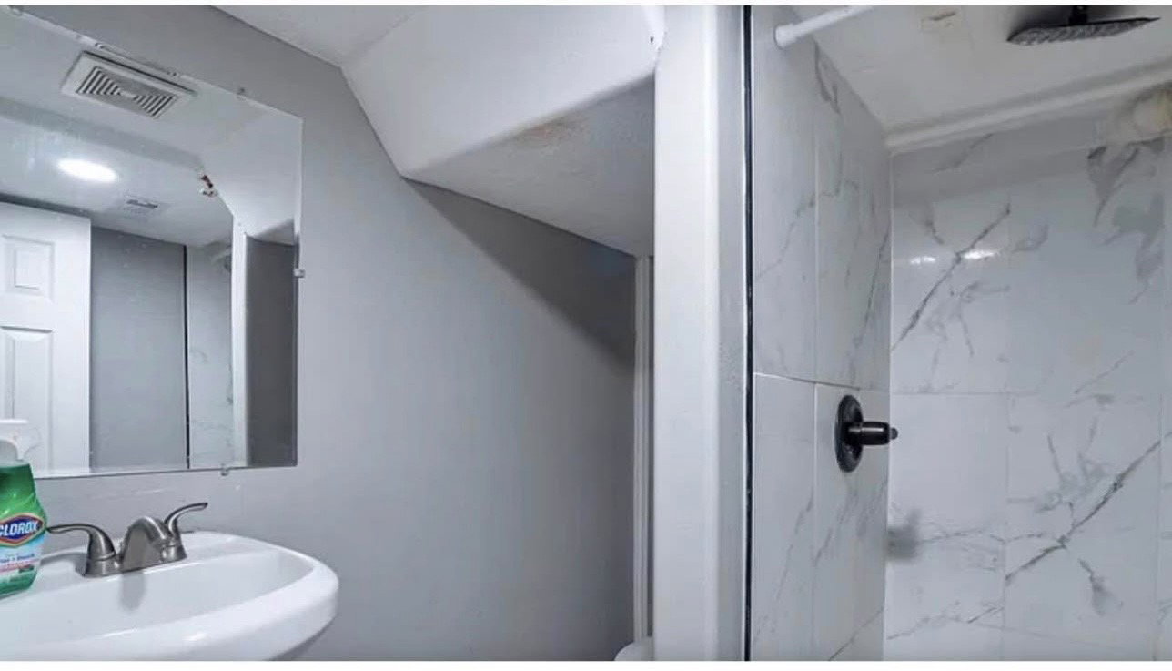 Bathroom featuring a white ceramic sink, a polished chrome faucet, a wall-mounted mirror, and a shower with white veined tile