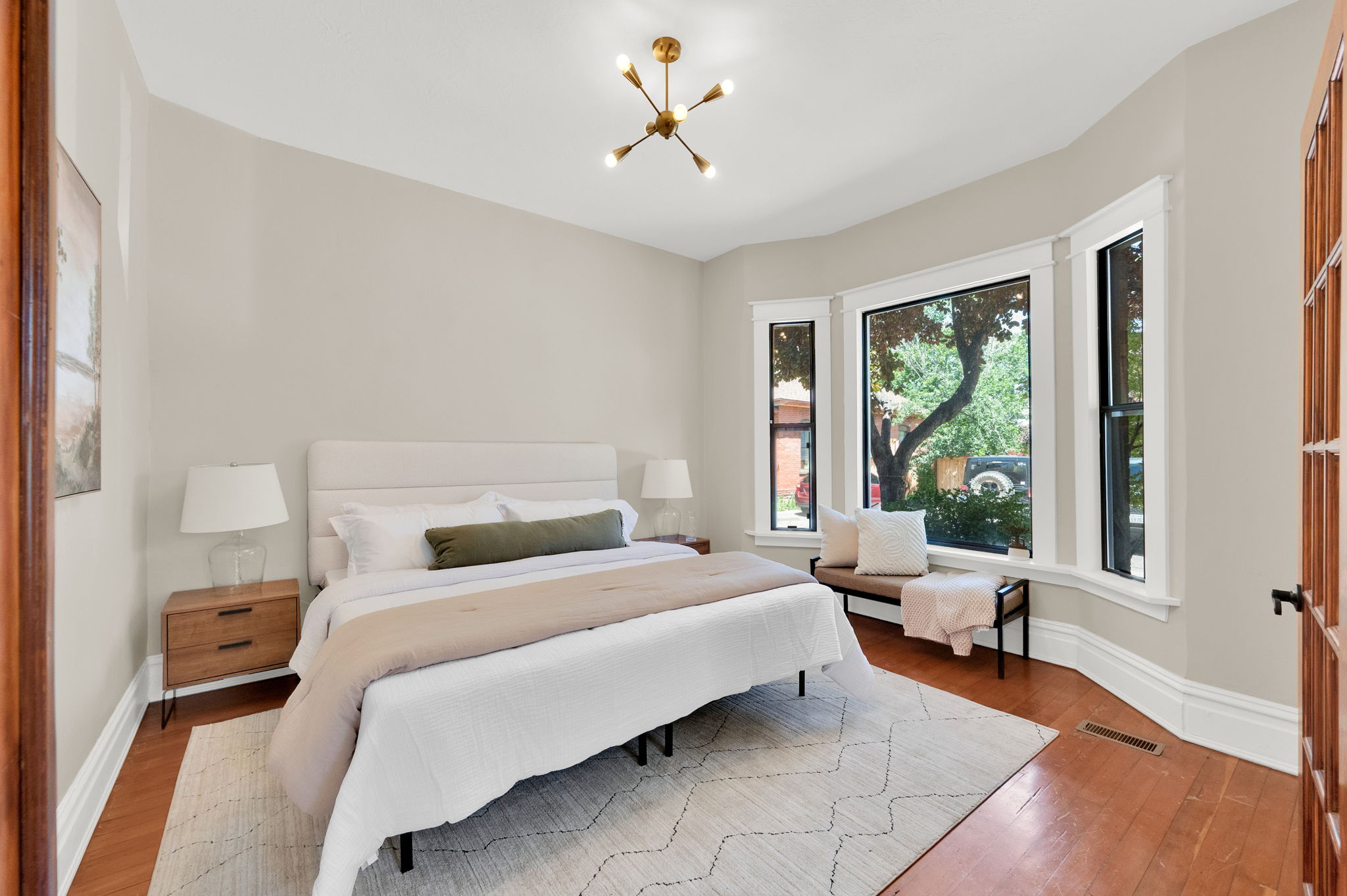 Bright bedroom featuring a bay window, hardwood flooring, and a modern ceiling light fixture