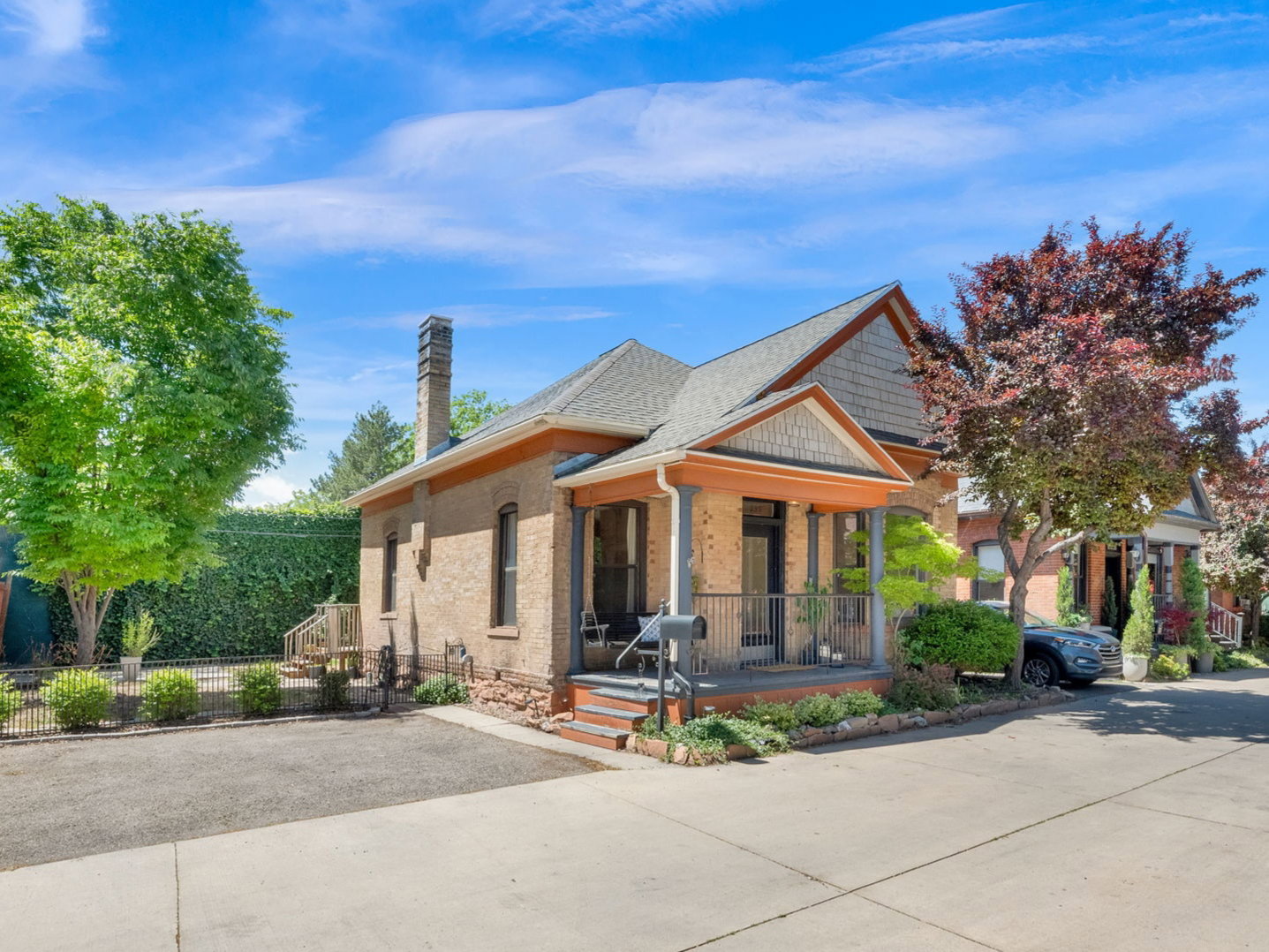 Brick exterior featuring a covered front porch, wood-finish columns, a pitched roofline, and mature landscaping