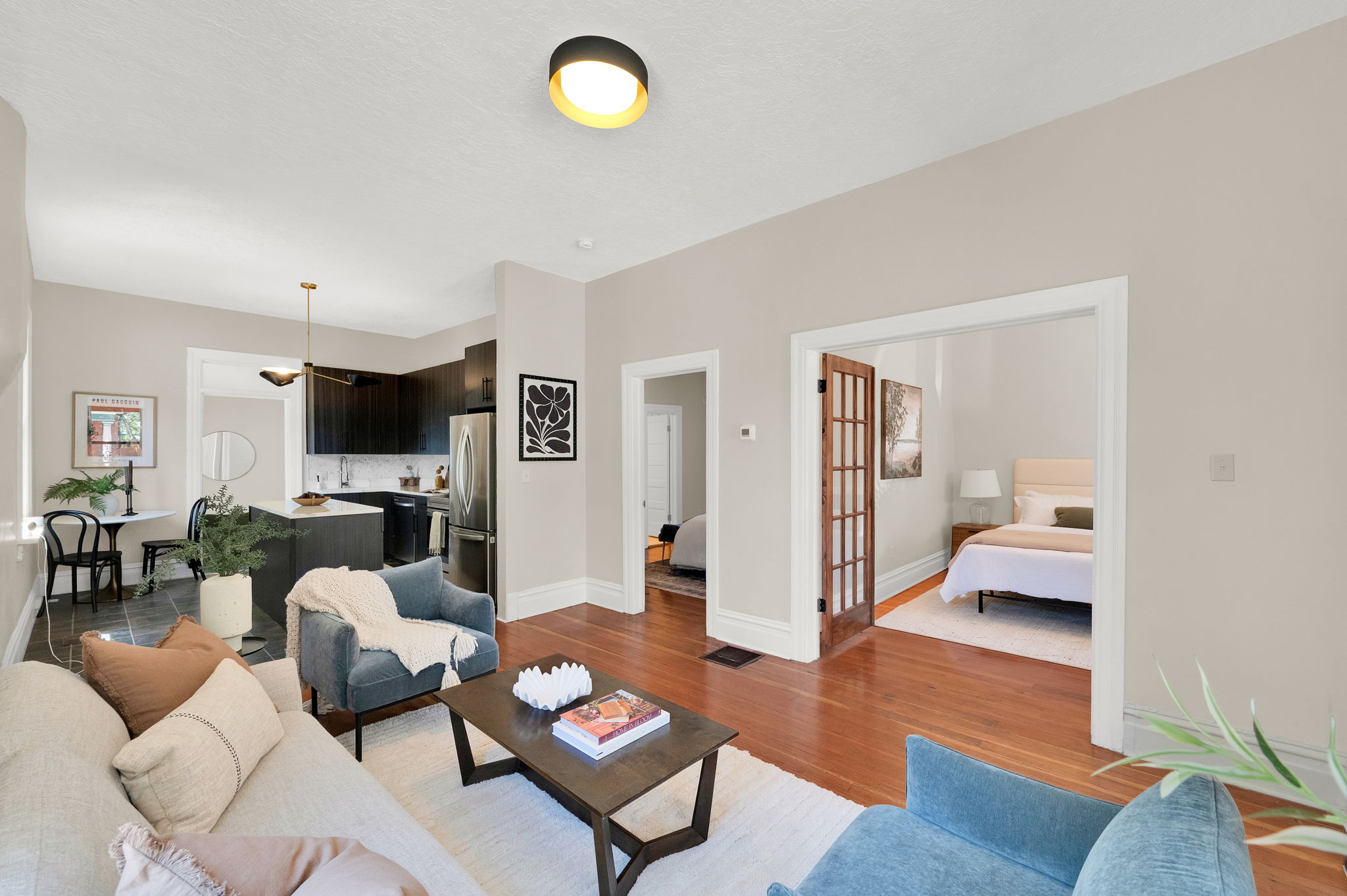 Open-concept living area with hardwood flooring, a modern kitchen featuring dark cabinetry and an island, and white trim throughout