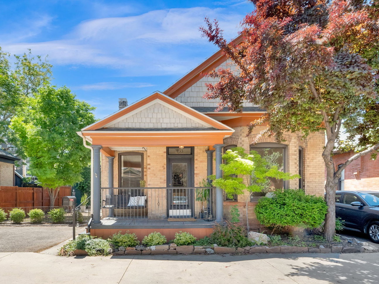 Brick exterior featuring a covered front porch with dark railings, a prominent gable with decorative shingles, and established landscaping