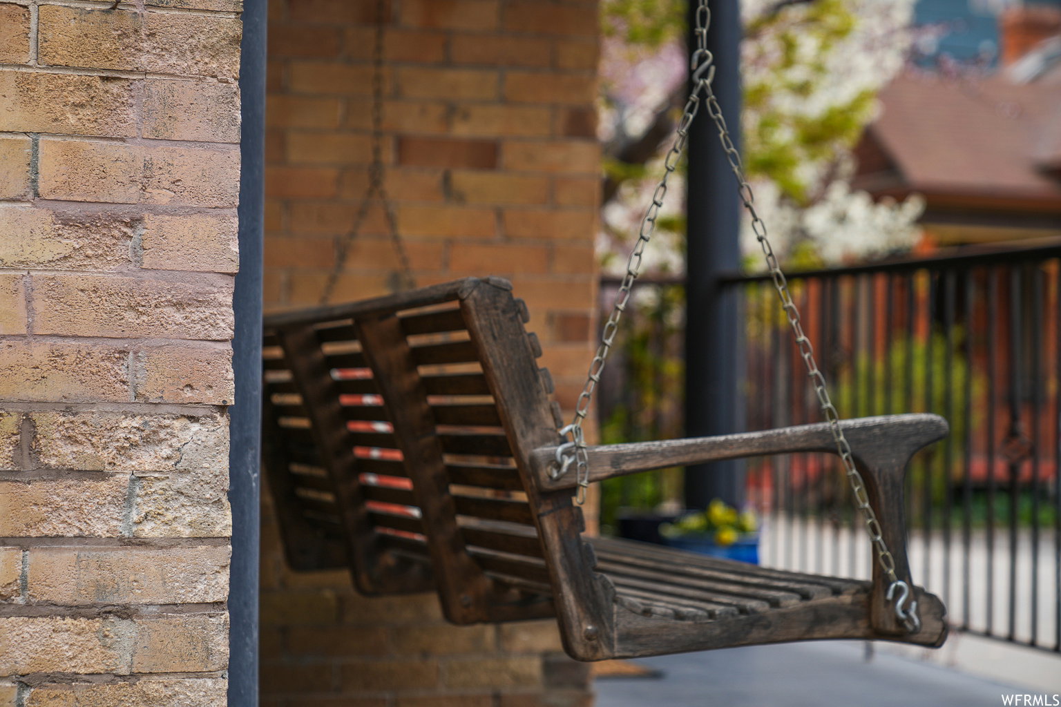 Covered porch featuring a slatted wood porch swing, brick exterior accents, and a black metal railing