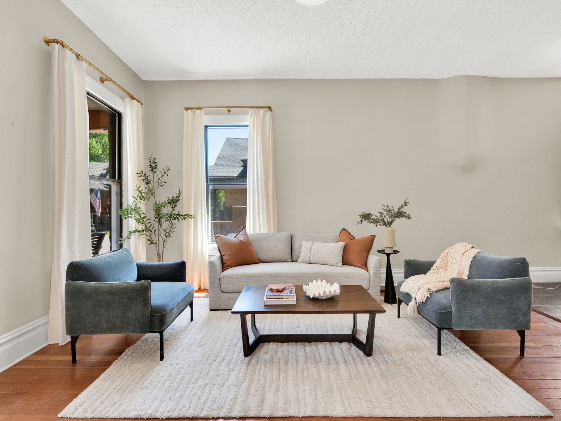 Living area with warm wood-finish flooring, light neutral wall tones, and tall windows