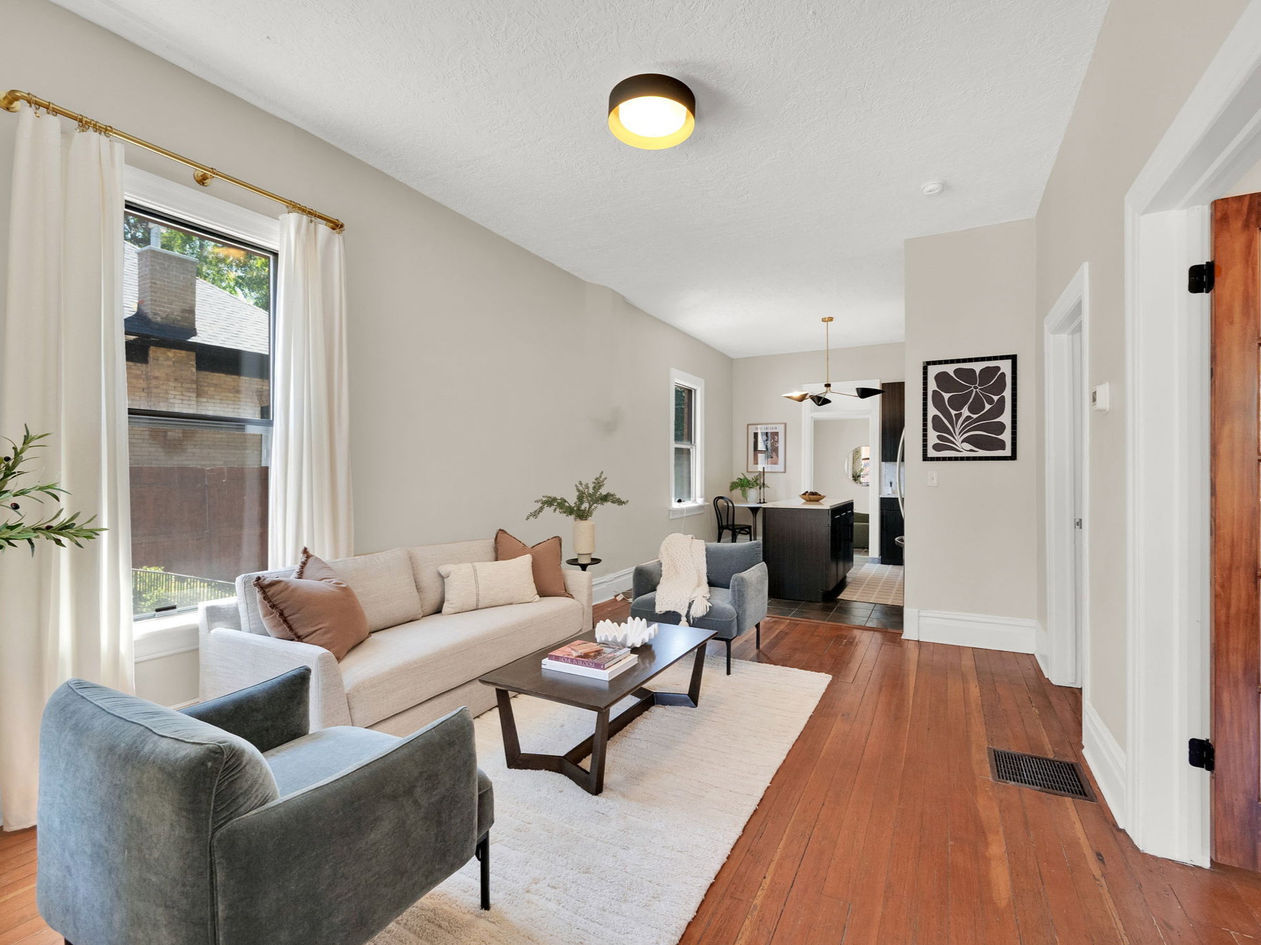 Spacious living area featuring rich hardwood flooring, neutral wall tones, and a modern flush-mount ceiling light