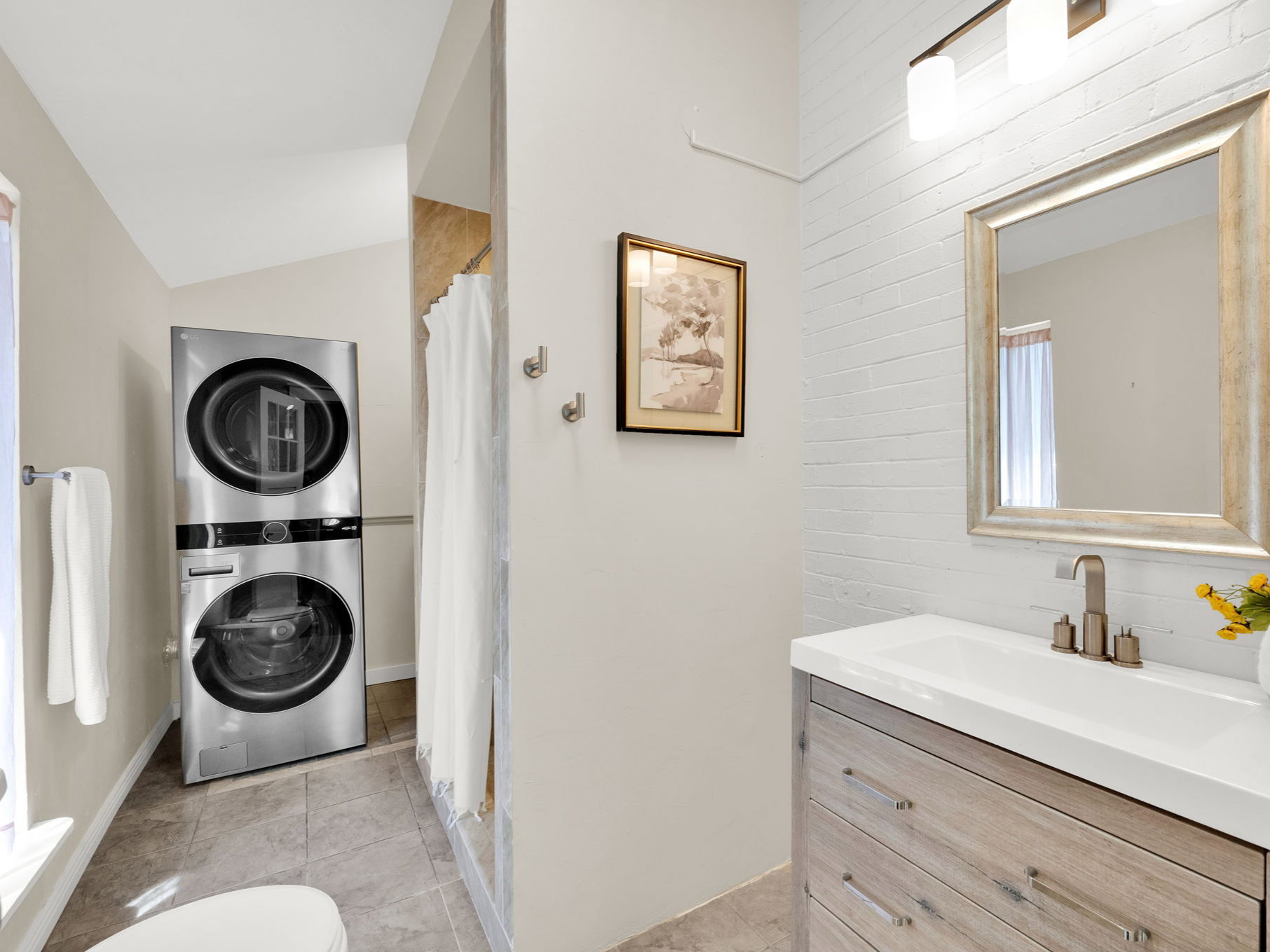 Bathroom featuring a stacked washer and dryer, vanity with a rectangular sink, brushed nickel faucet, and a framed mirror