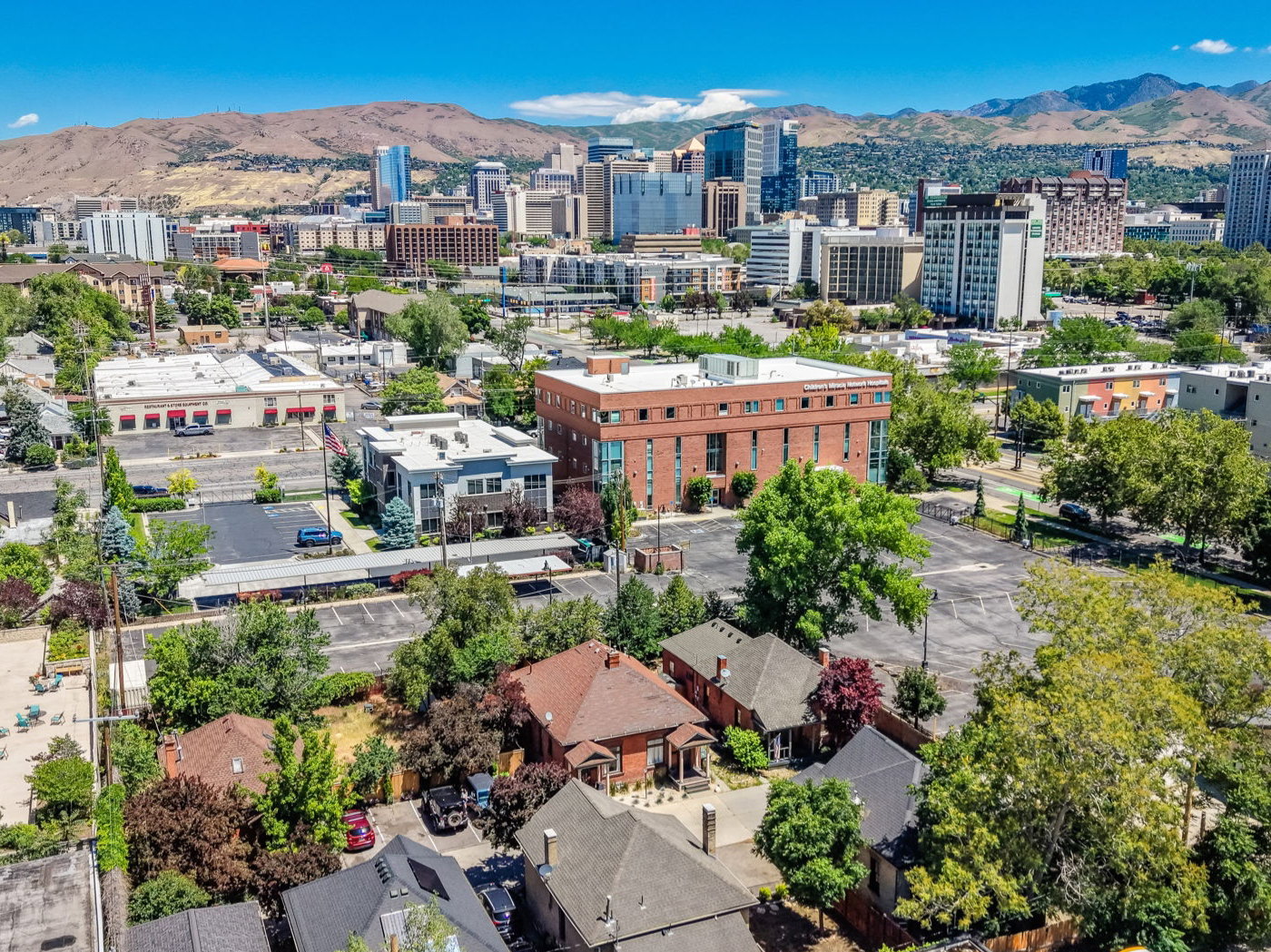 Urban setting featuring a diverse architectural landscape with commercial and residential structures, mature trees, and mountainous backdrop