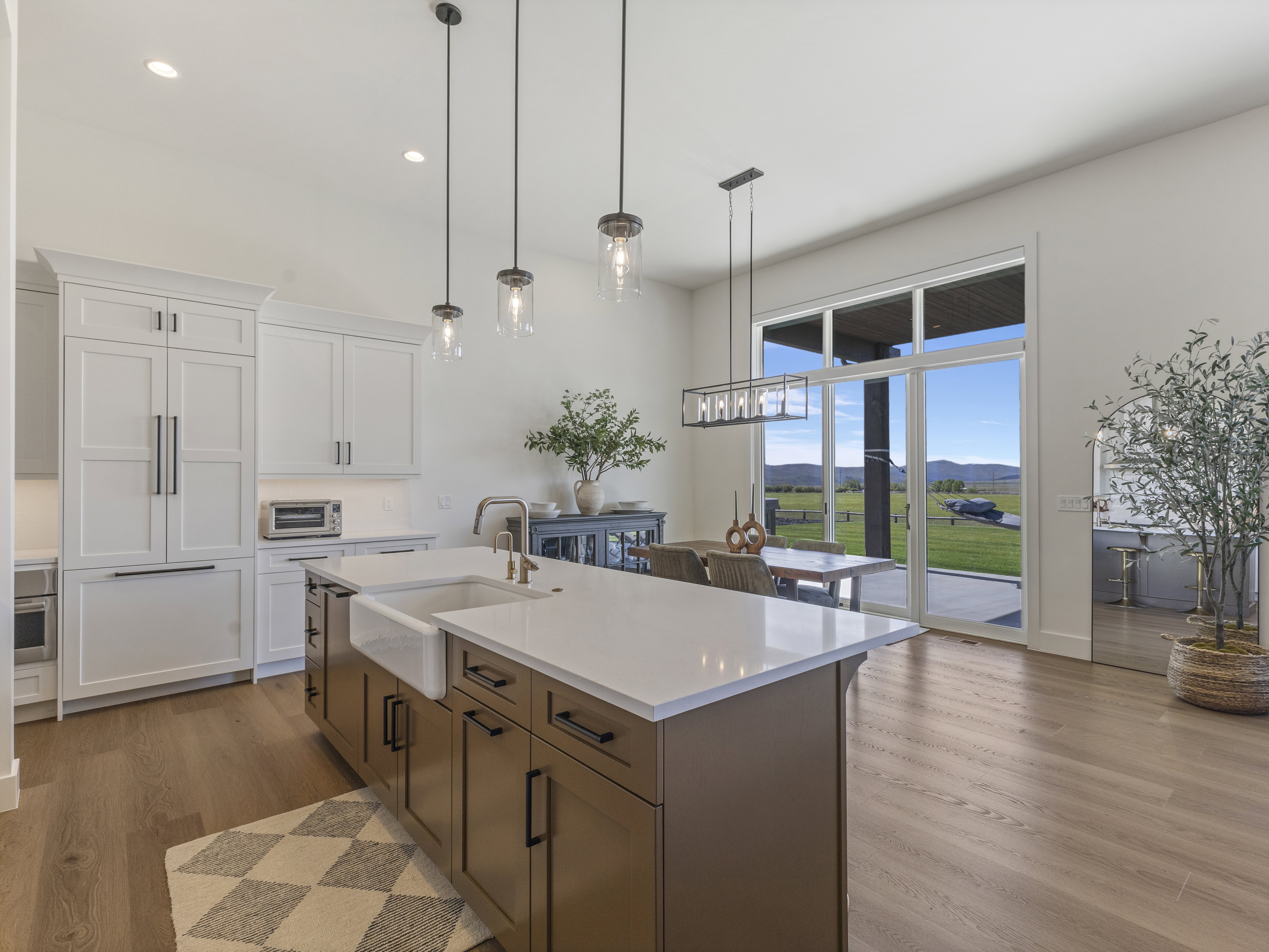 Open-concept kitchen and dining area featuring a large center island with a farmhouse sink and quartz countertop, integrated refrigerator, pendant lighting, and wood-finish flooring