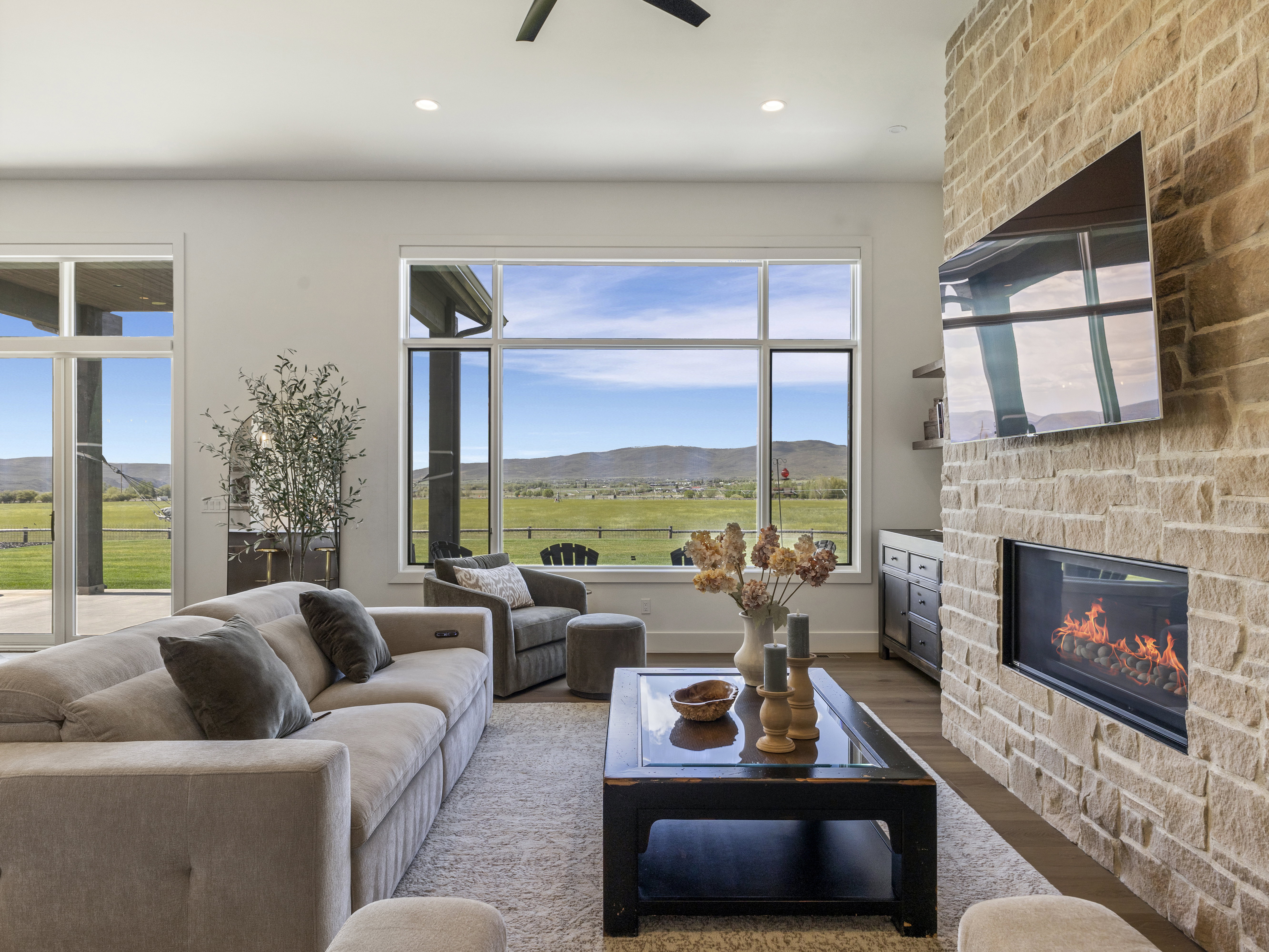 Living area featuring a floor-to-ceiling stone fireplace, expansive windows, sliding glass doors, a built-in linear fireplace, and wood-finish flooring