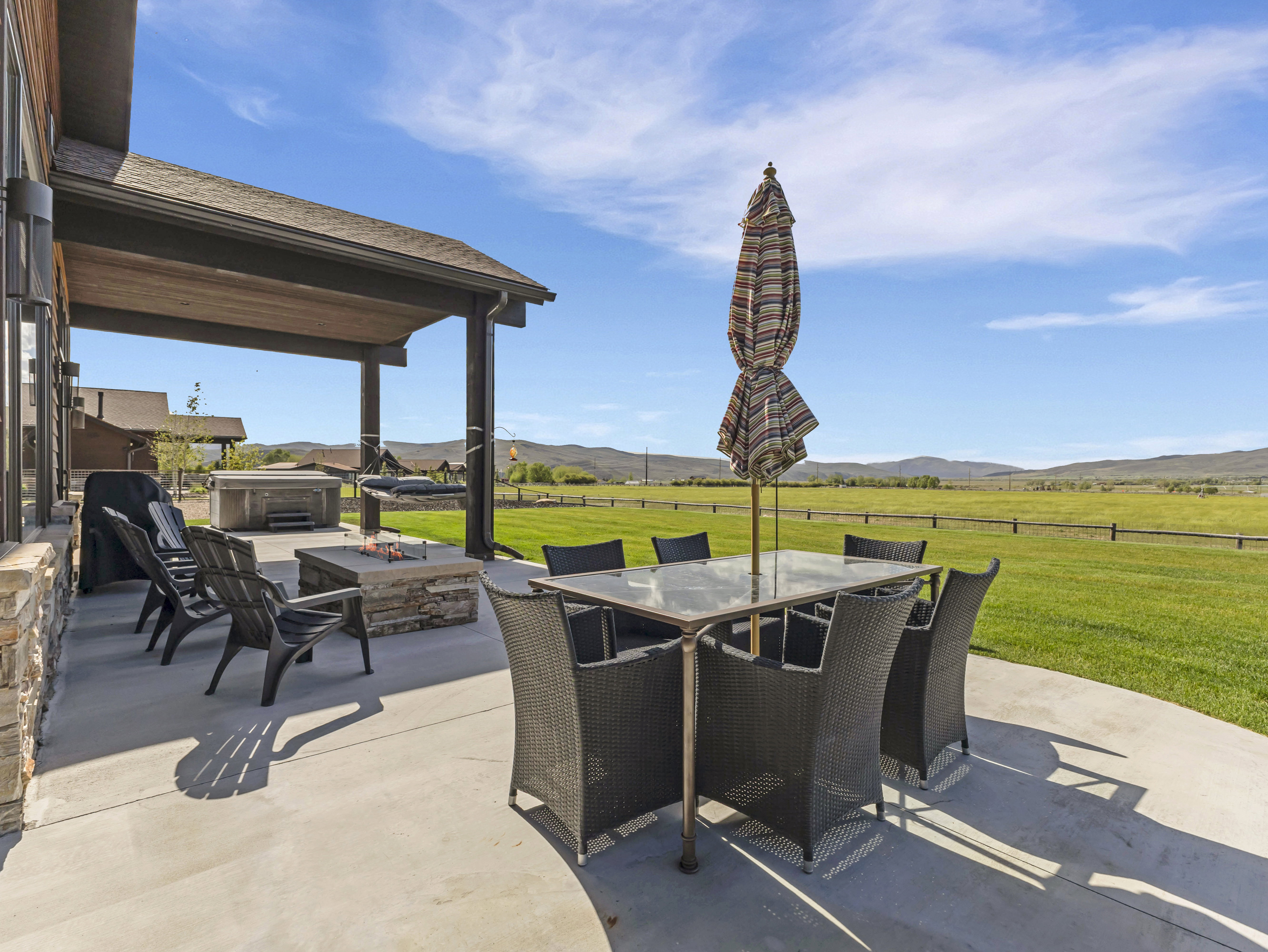 Expansive concrete patio featuring a stone-clad fire pit, covered outdoor living space, and a hot tub