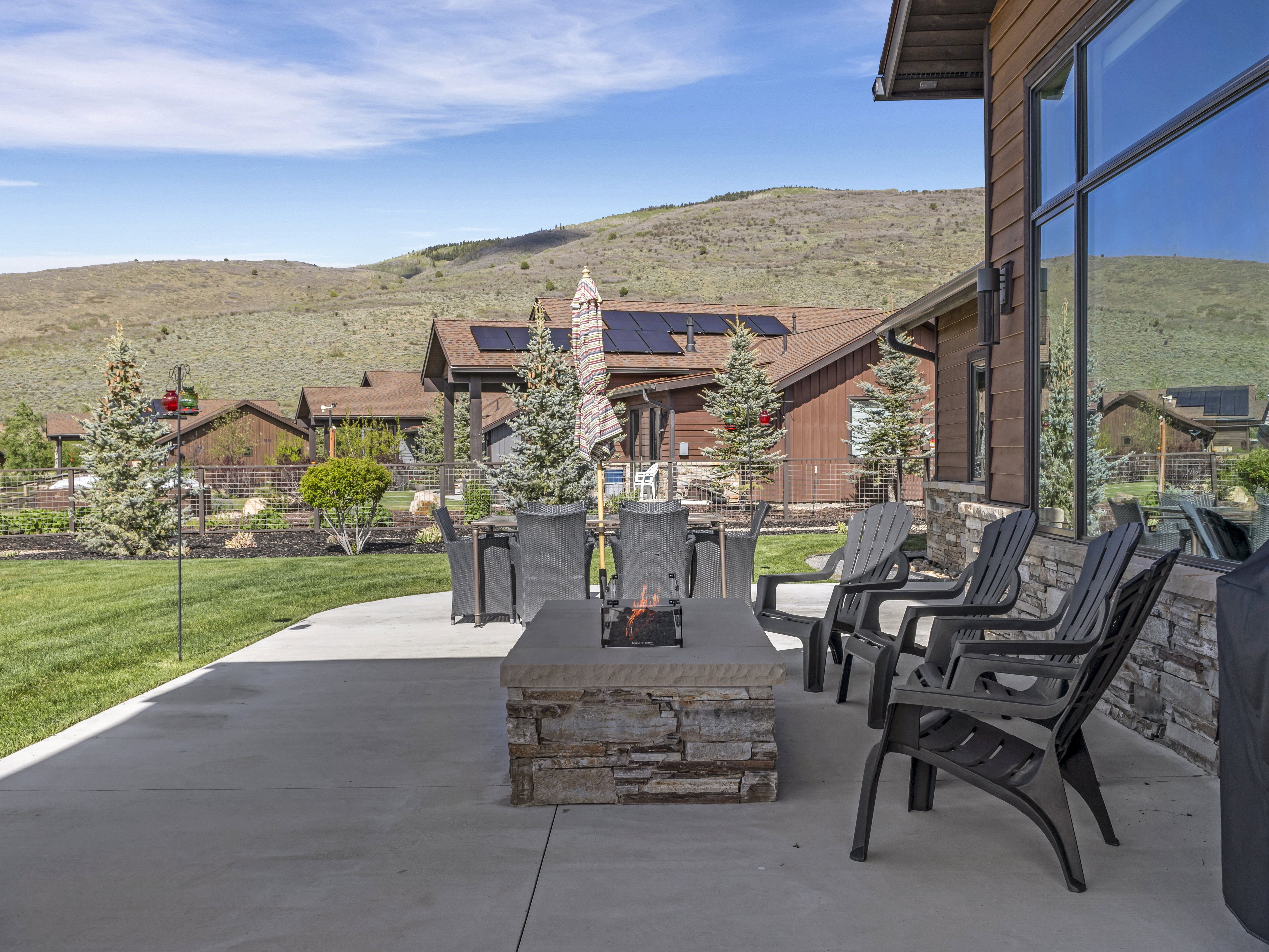 Spacious concrete patio featuring a stacked stone fire pit, extensive lawn area, and mature evergreen landscaping
